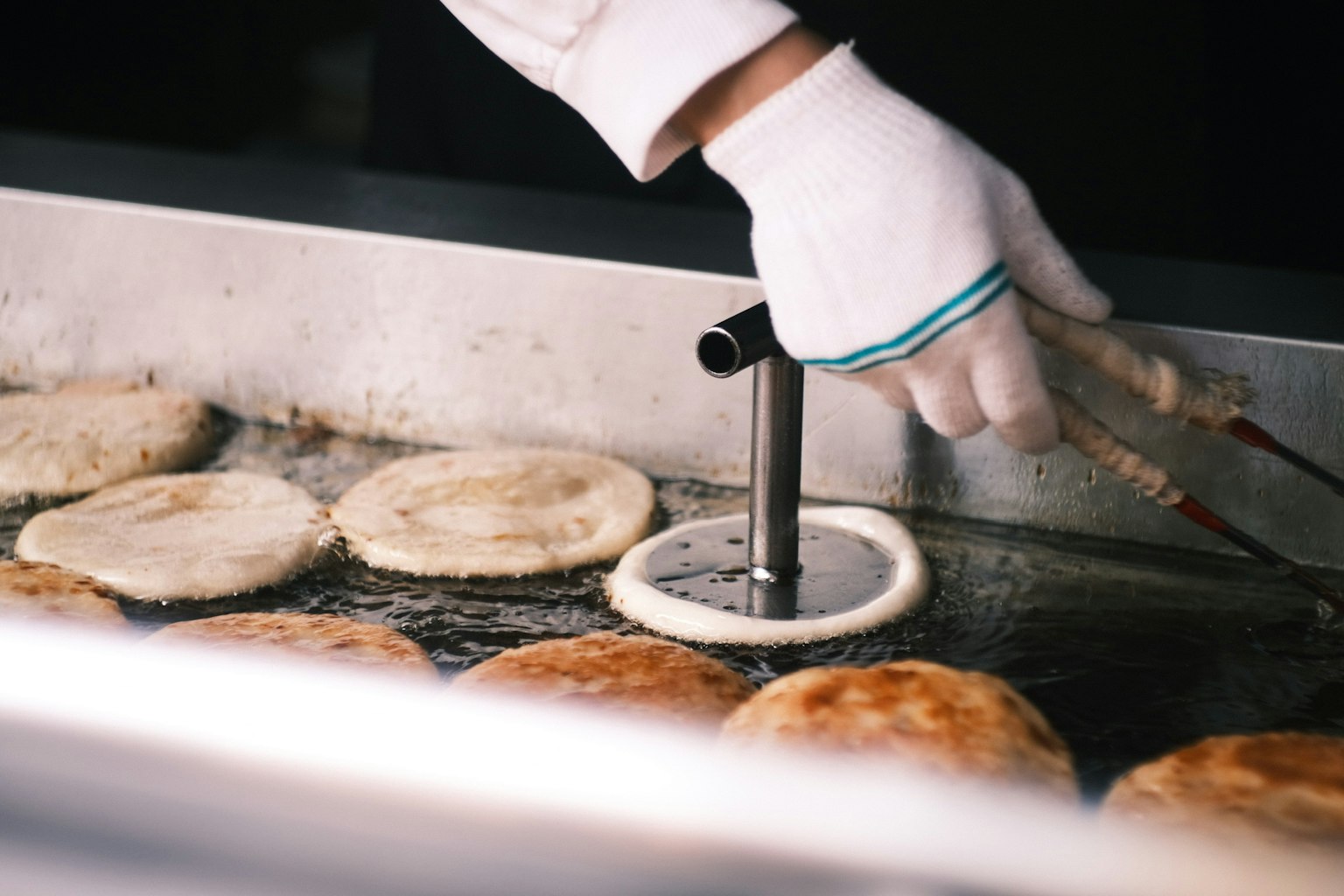 Una mano che cucina pancake su una piastra con delle pinze