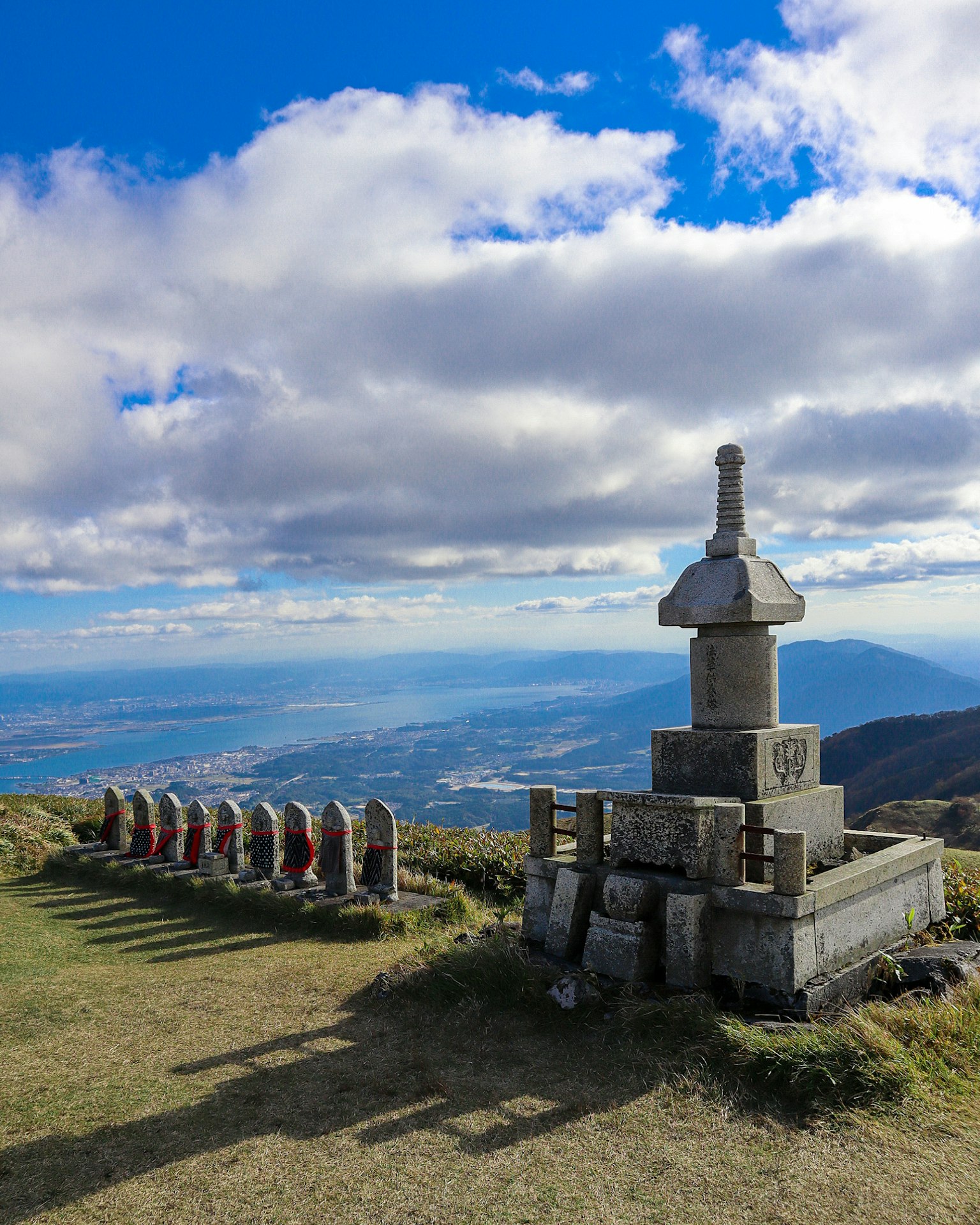 Stone monument with offerings at a mountain peak overlooking a valley