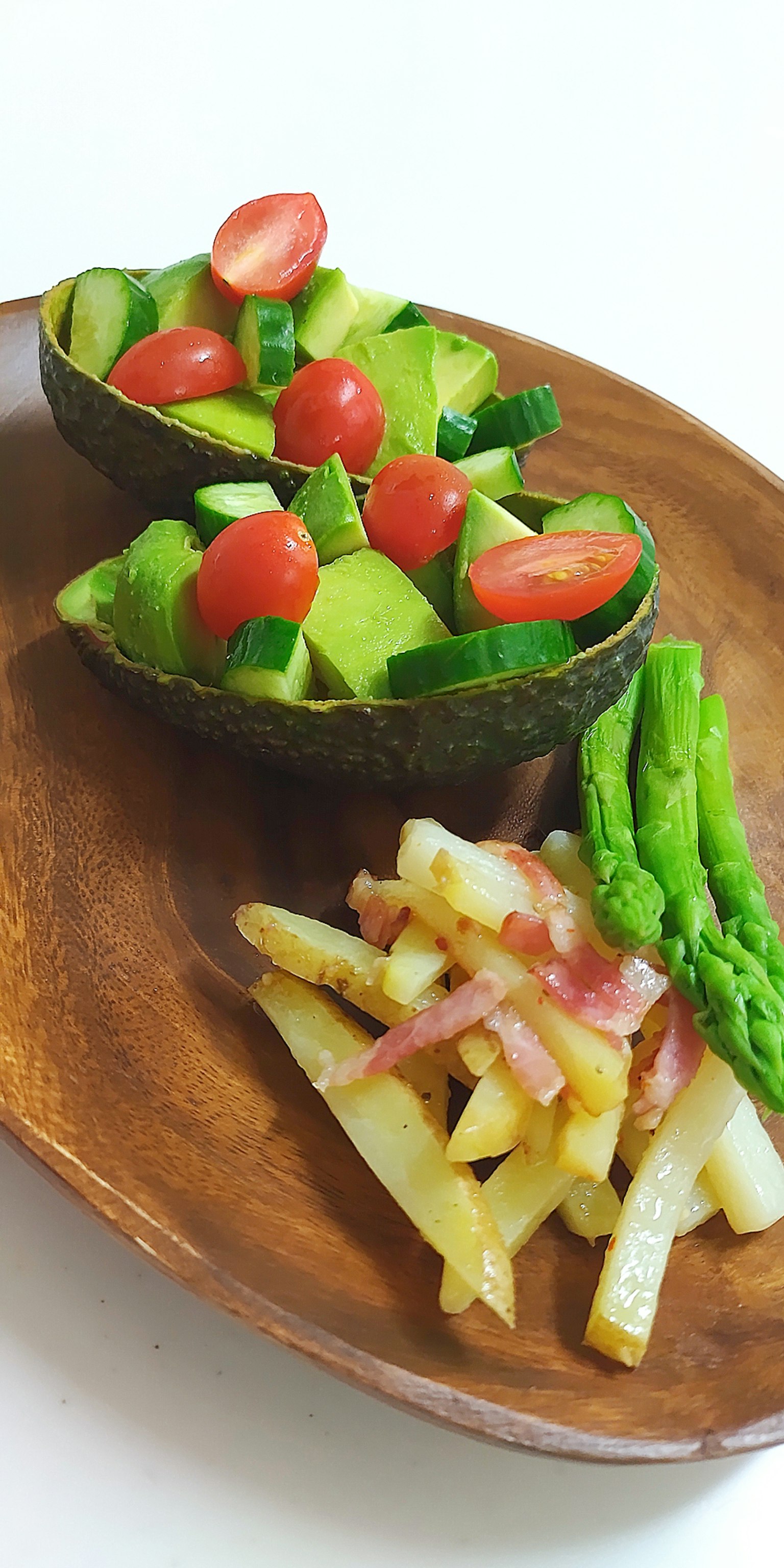 Ciotole di avocado con insalata di pomodori e cetrioli insieme ad asparagi e patatine fritte