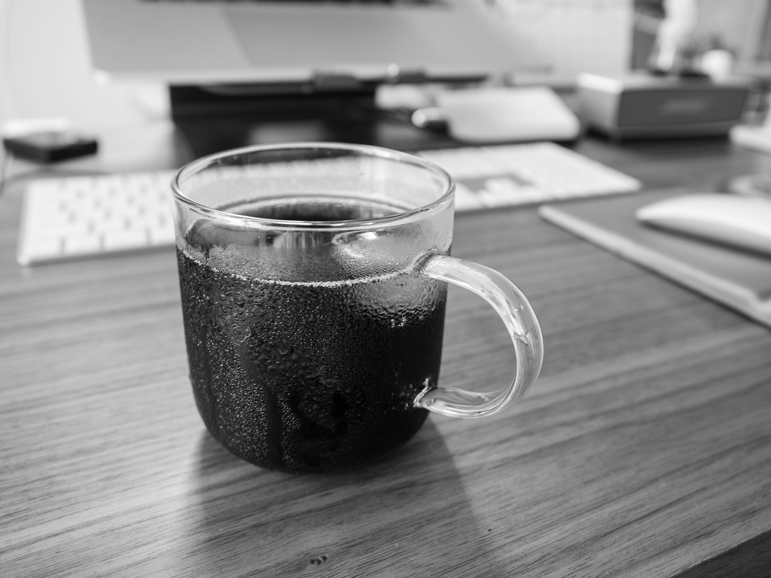 Una tazza di vetro trasparente piena di caffè nero su un tavolo di legno