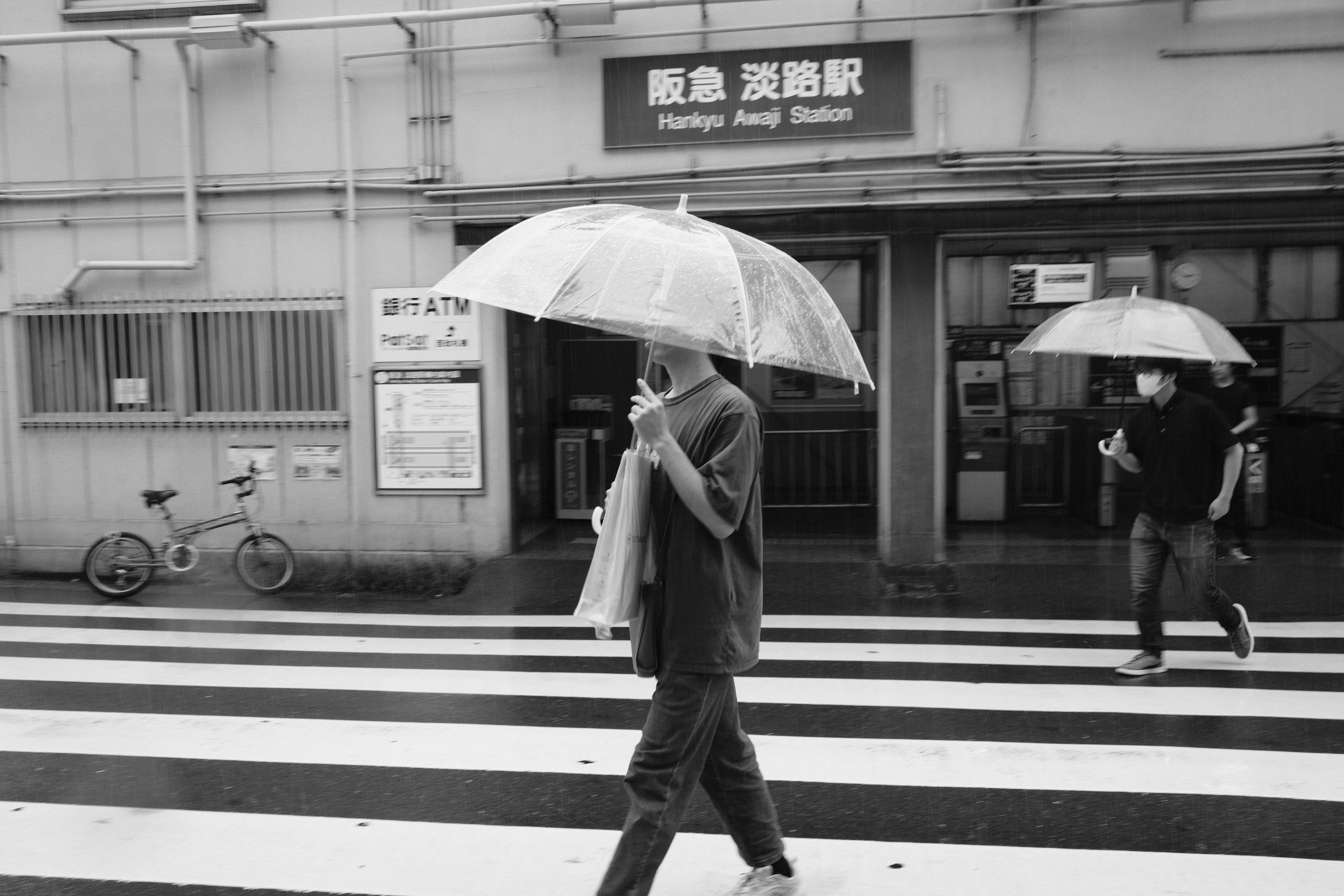 người cầm ô băng qua đường trước nhà ga