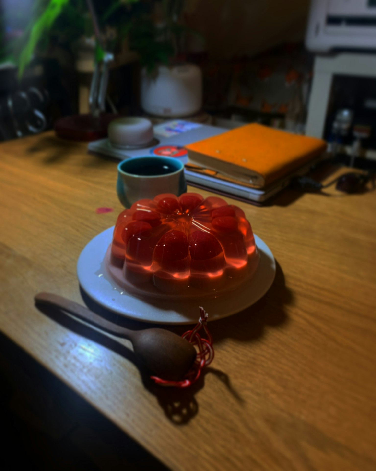 Rote Gelee auf einem weißen Teller mit einem Holzlöffel warmes Getränk und Bücher im Hintergrund