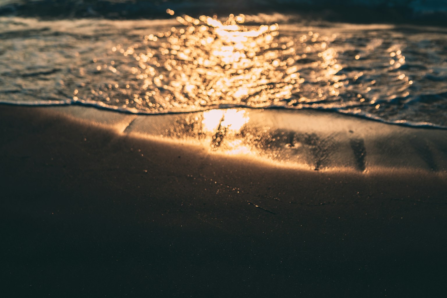 Wellen an einem Sandstrand mit Sonnenreflexion