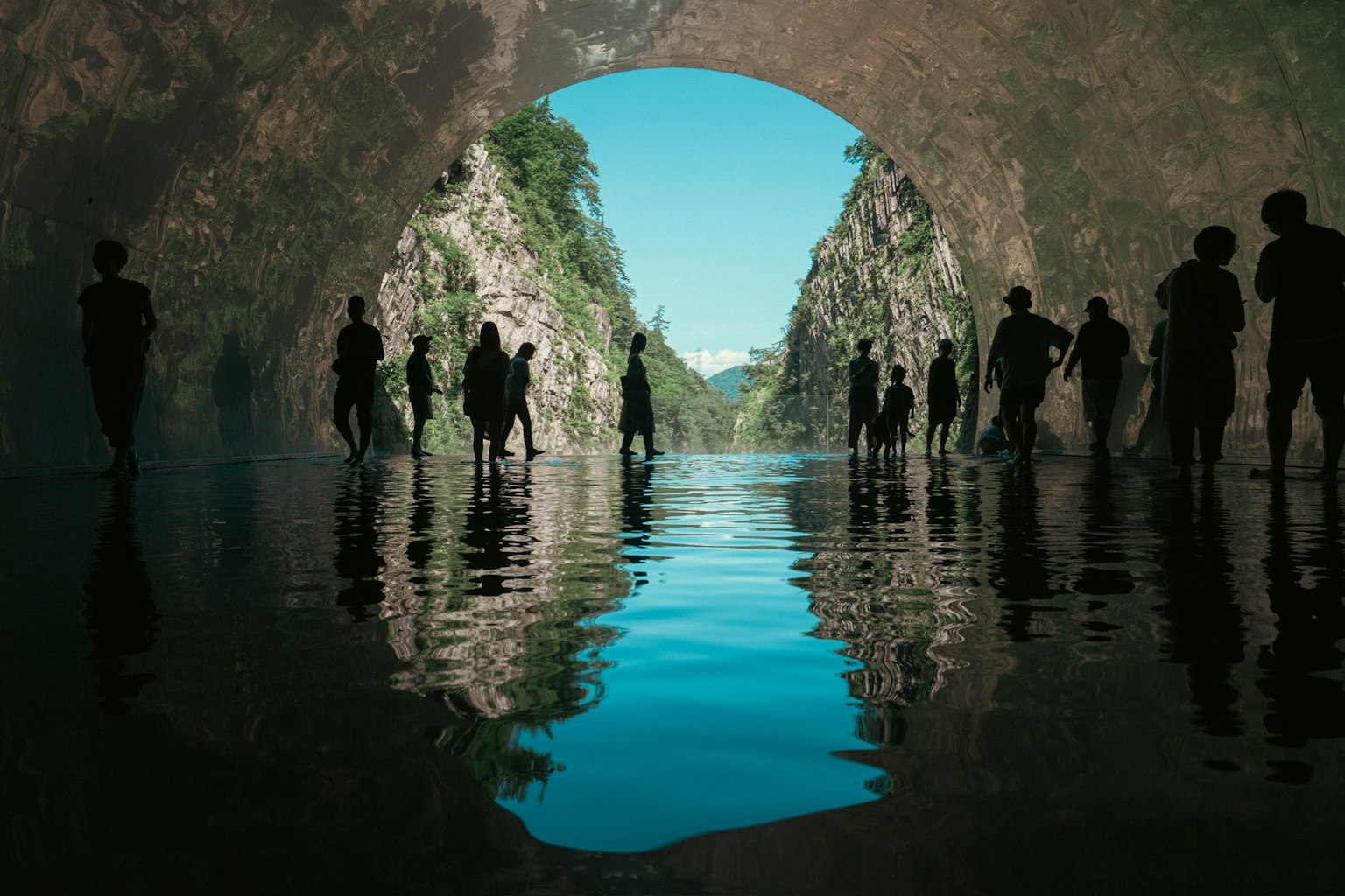 水面に映る人々のシルエットと青空のトンネル