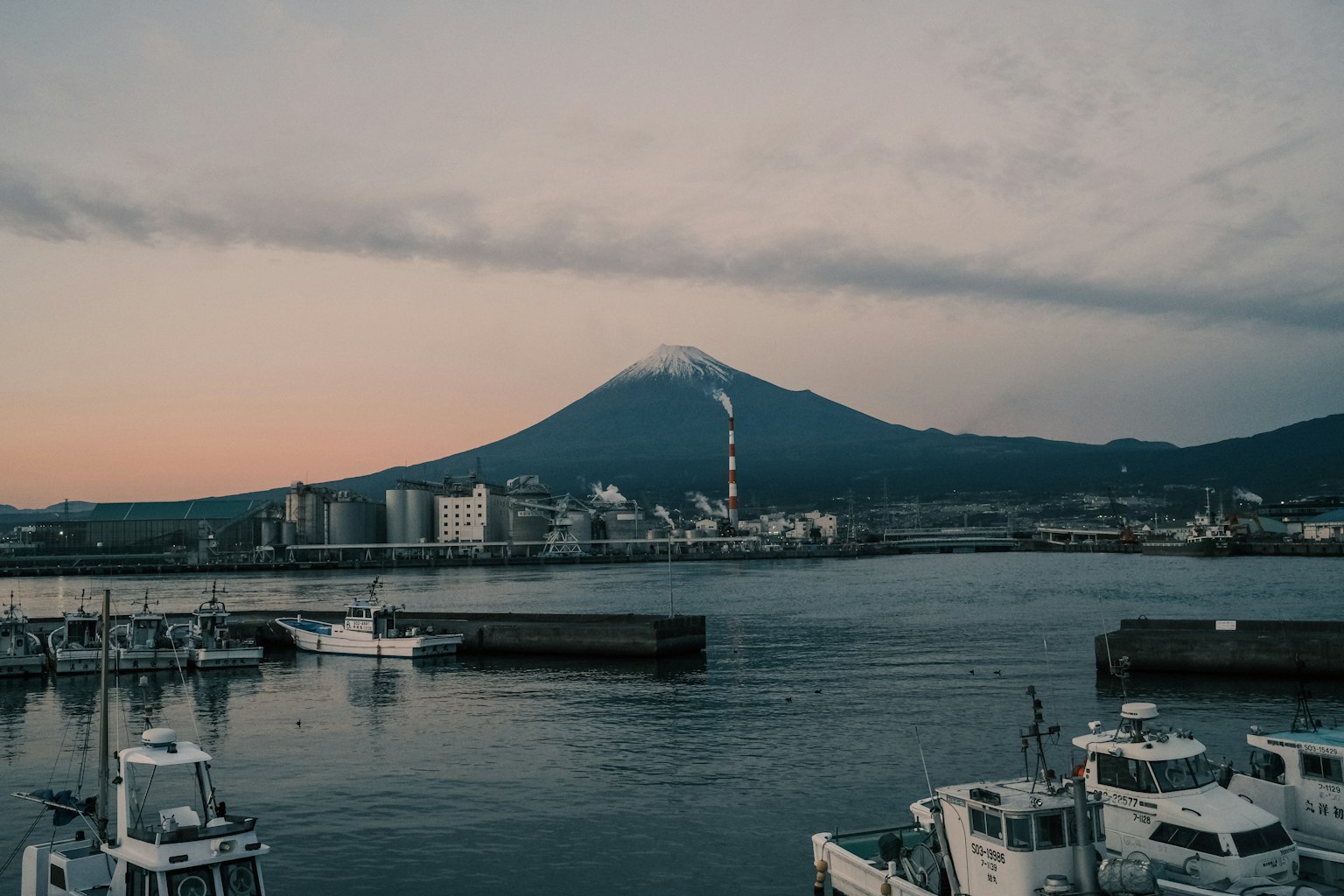 Vue du port avec le mont Fuji en arrière-plan et des bateaux et des usines le long de la mer calme