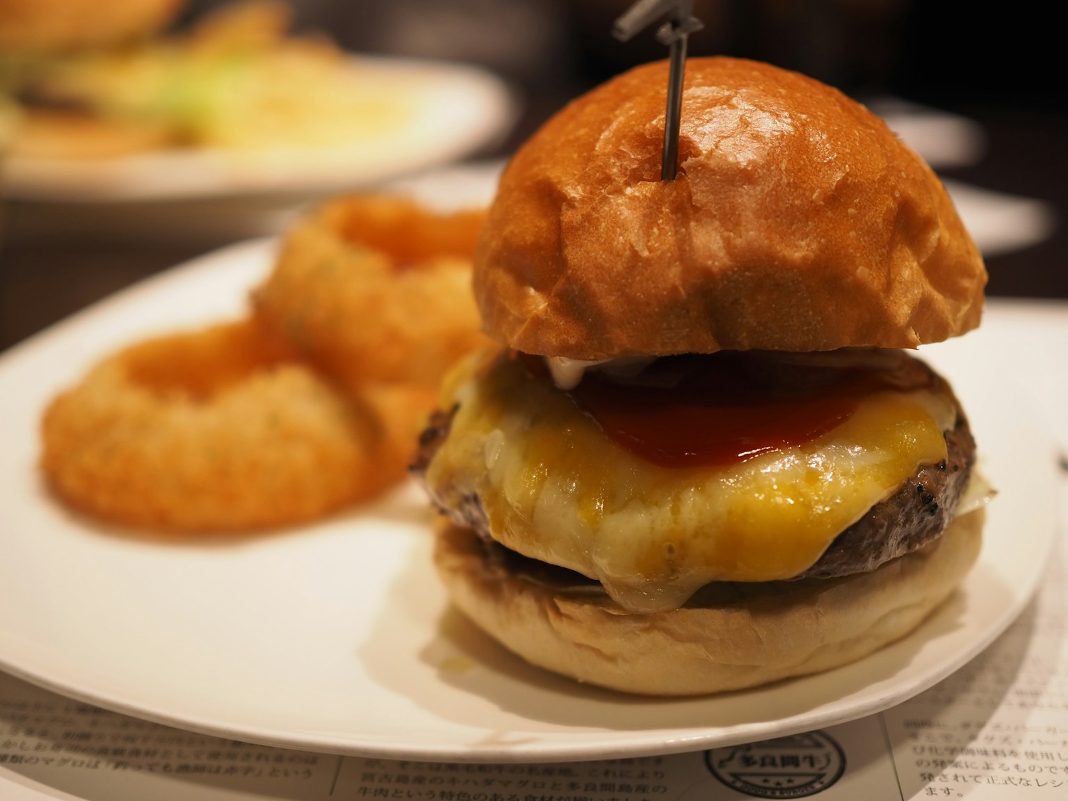 Acercamiento a una hamburguesa con queso derretido y ketchup servida con aros de cebolla