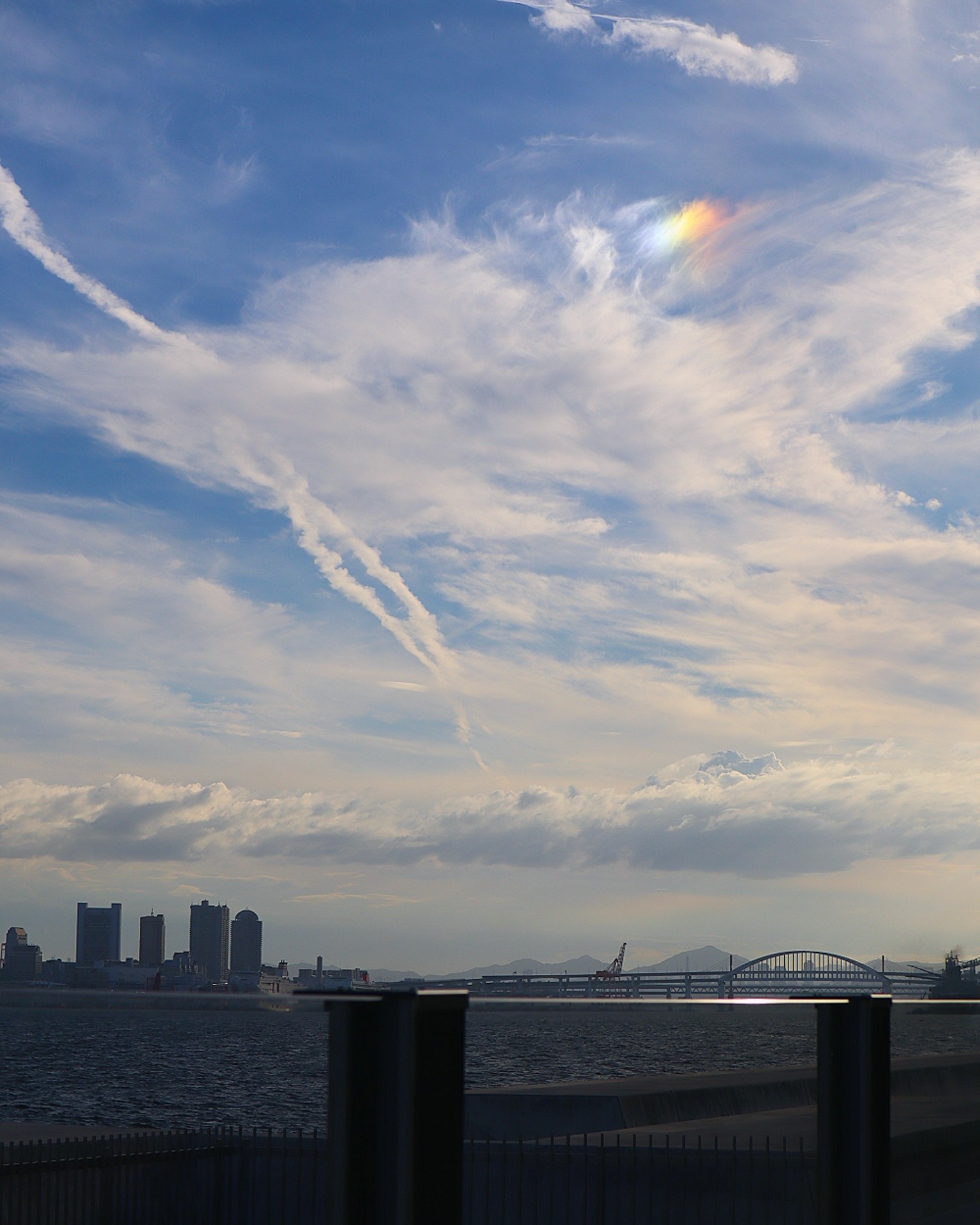 Coastal view featuring a blue sky with clouds and a rainbow-like light streak