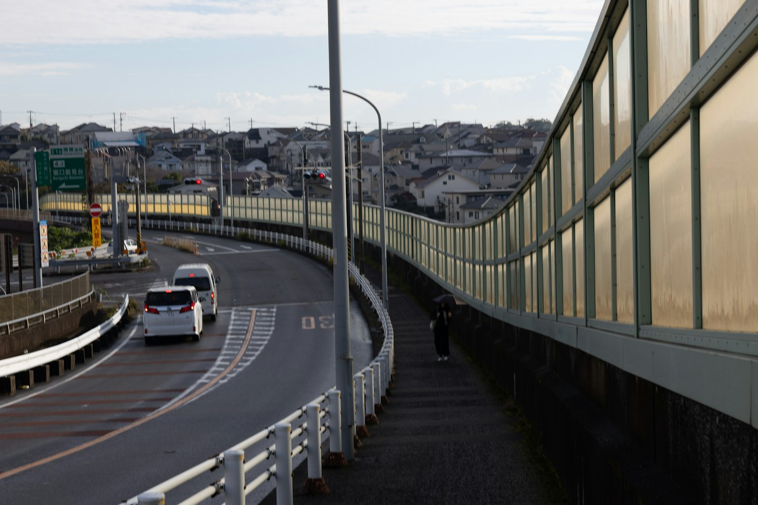 Una vista de una carretera con una acera al lado de coches circulando y edificios al fondo
