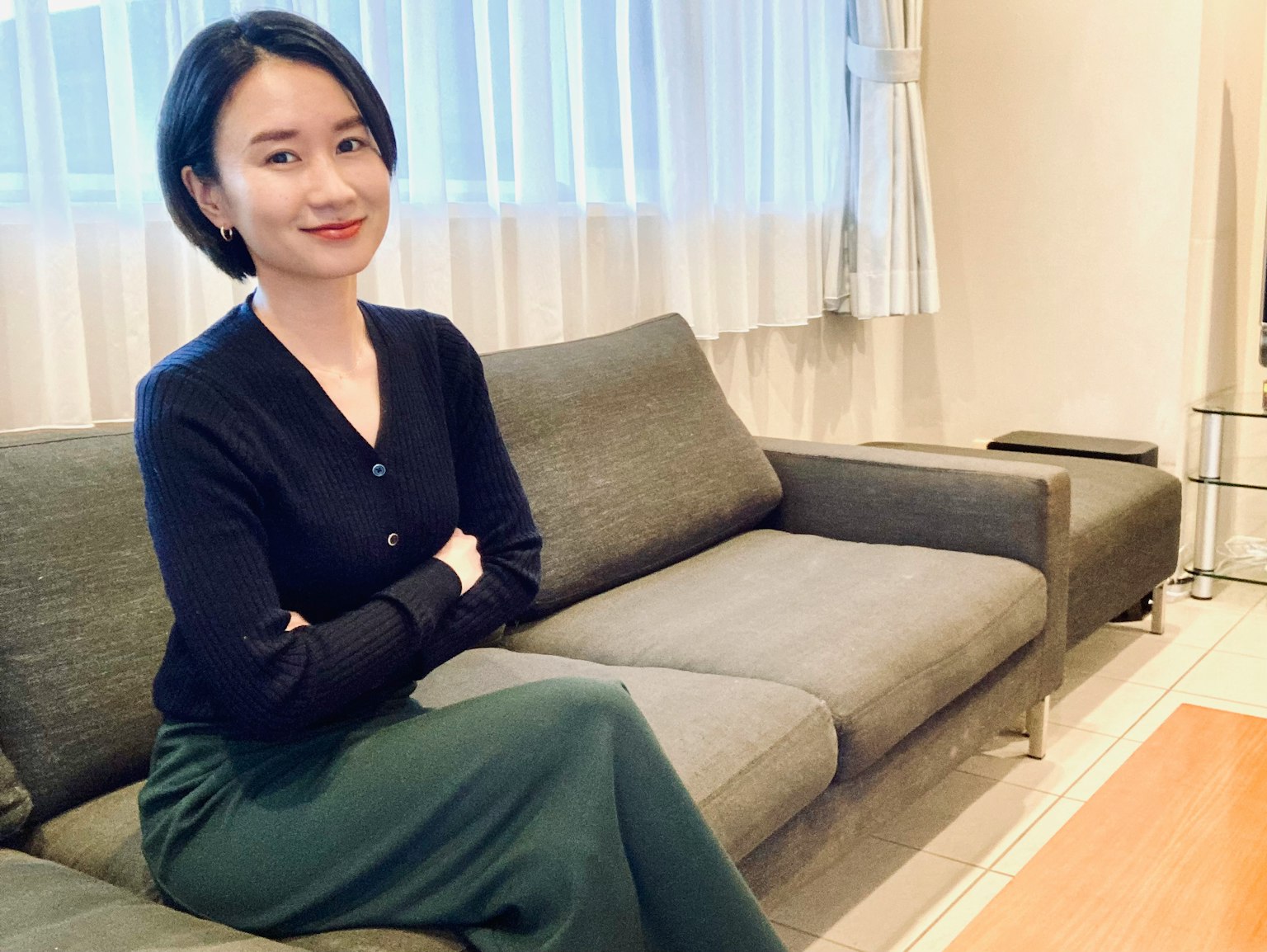소파에 앉아 있는 여성의 초상 짧은 검은 머리 회색 소파 밝은 커튼