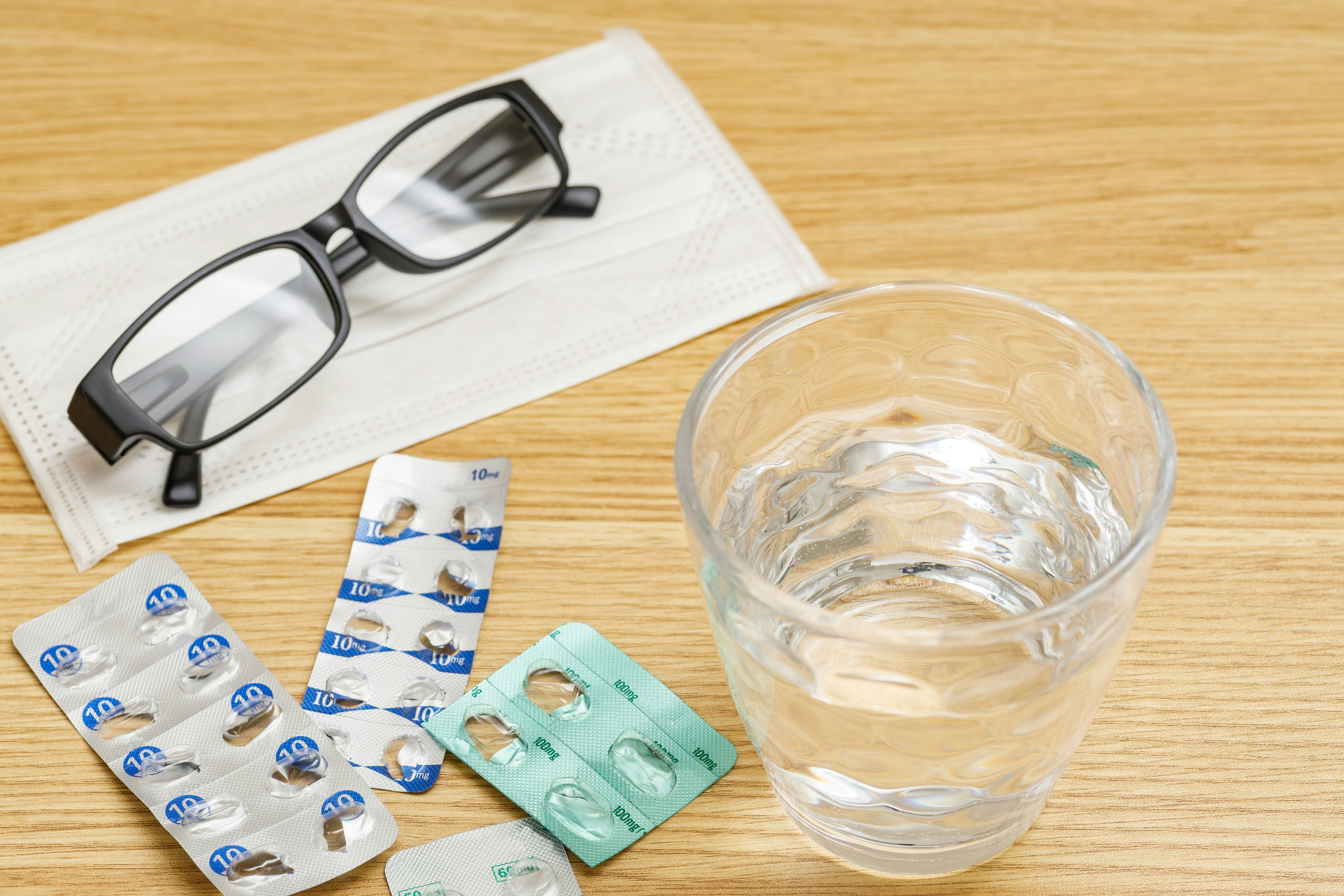 Glasses and a glass of water with pill packages on a wooden table