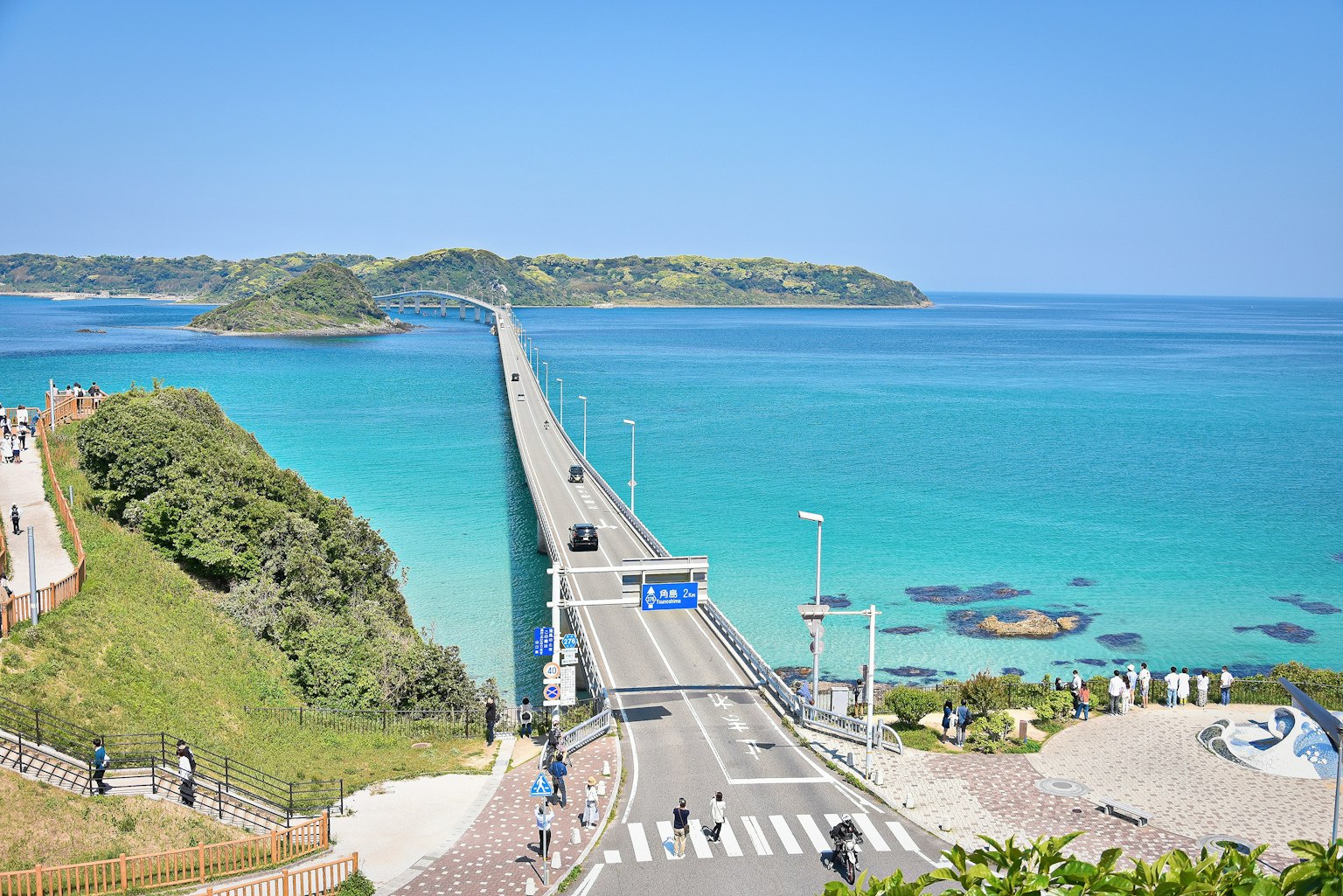 Scenic view of a blue ocean and a bridge with green hills and distant islands