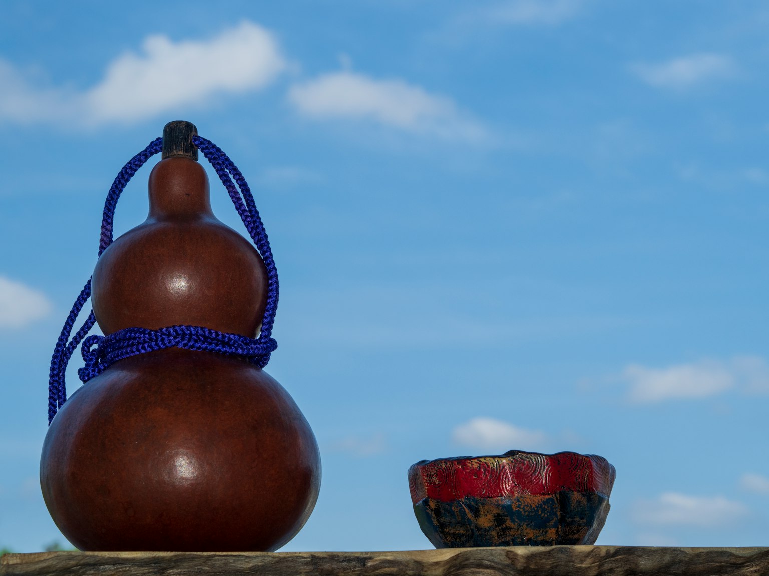Calabaza marrón con cuerda morada junto a un pequeño bol rojo bajo un cielo azul