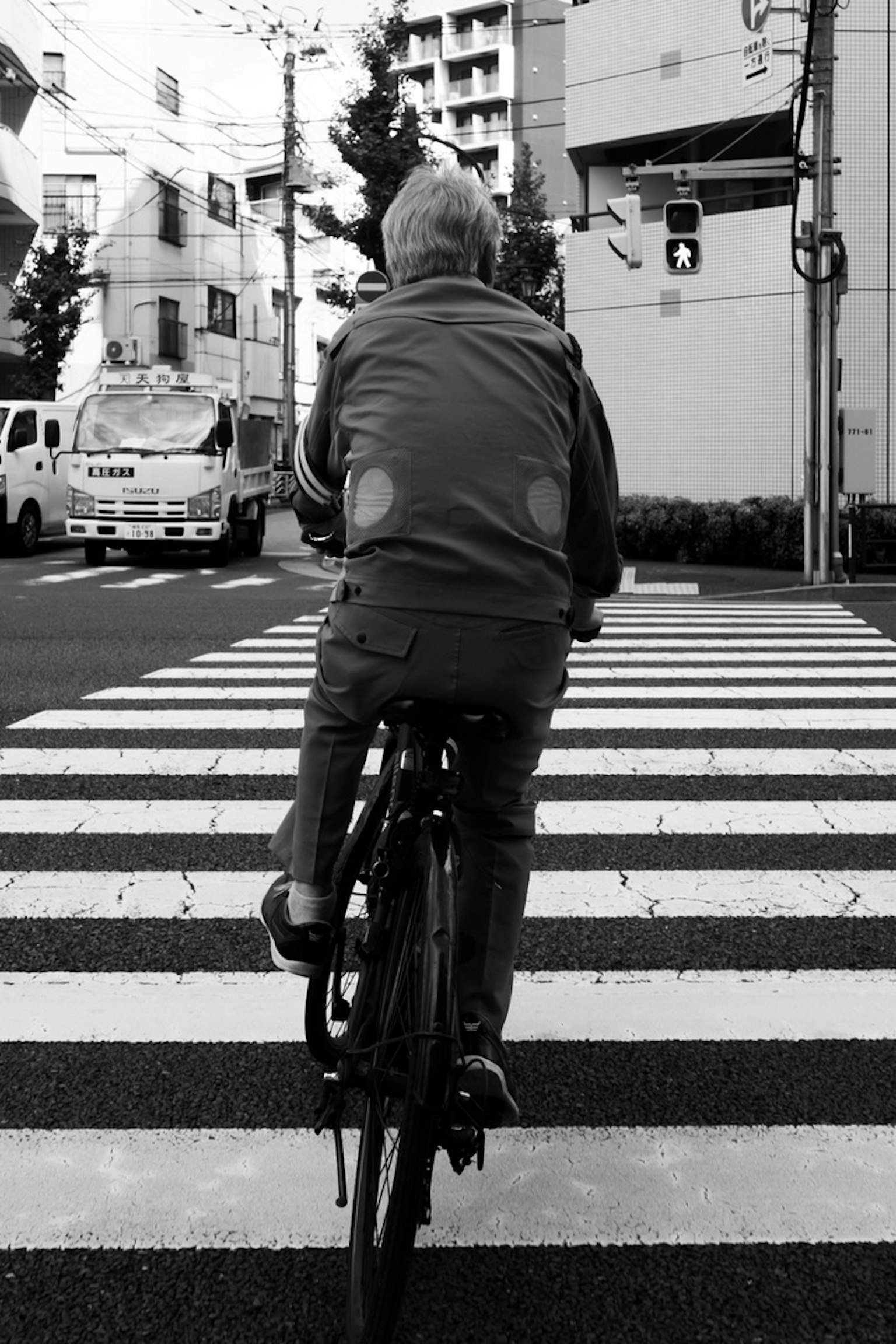 Persona anziana in bicicletta su un attraversamento pedonale in bianco e nero
