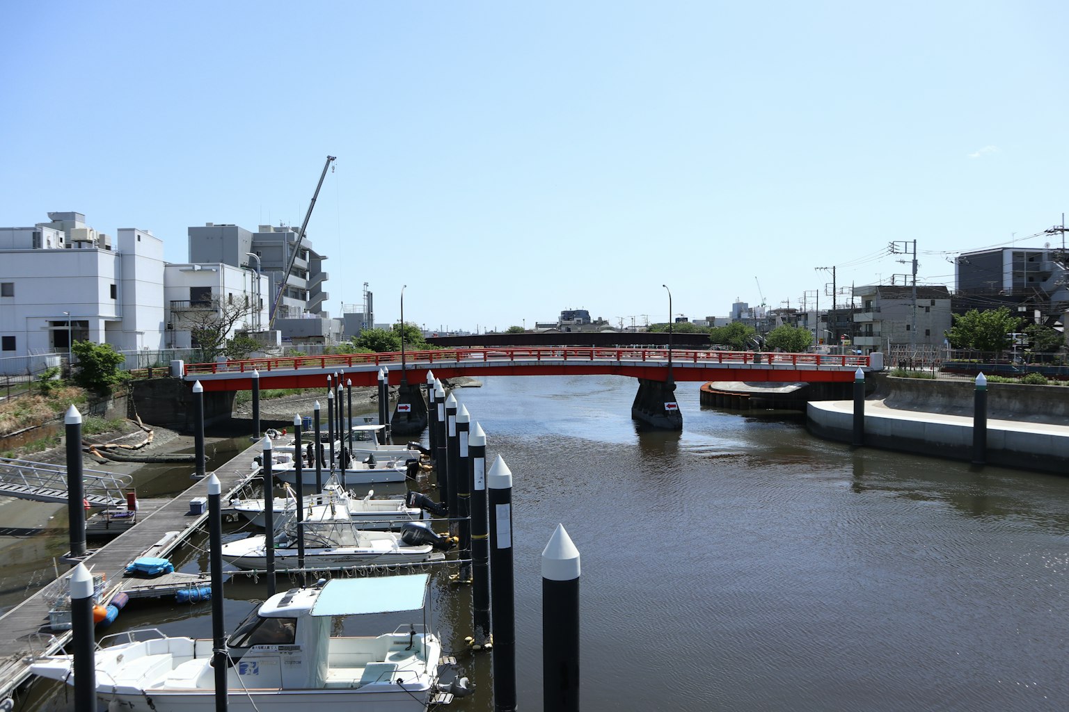 Blick auf eine rote Brücke über einen ruhigen Fluss mit Gebäuden und Booten in der Nähe