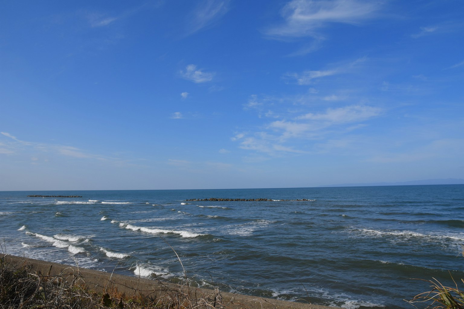 Lautan dan langit biru yang luas dengan ombak lembut menyapu pantai berpasir