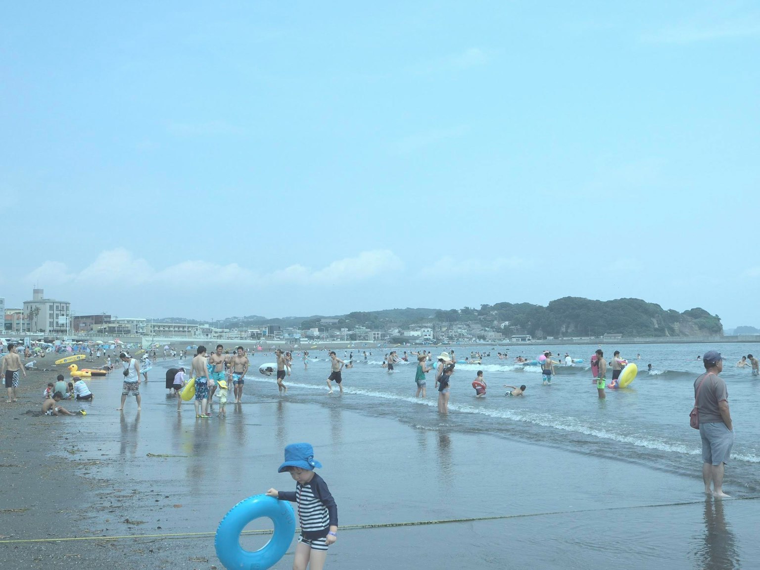 Children and adults enjoying a beach scene with a blue sky and calm sea