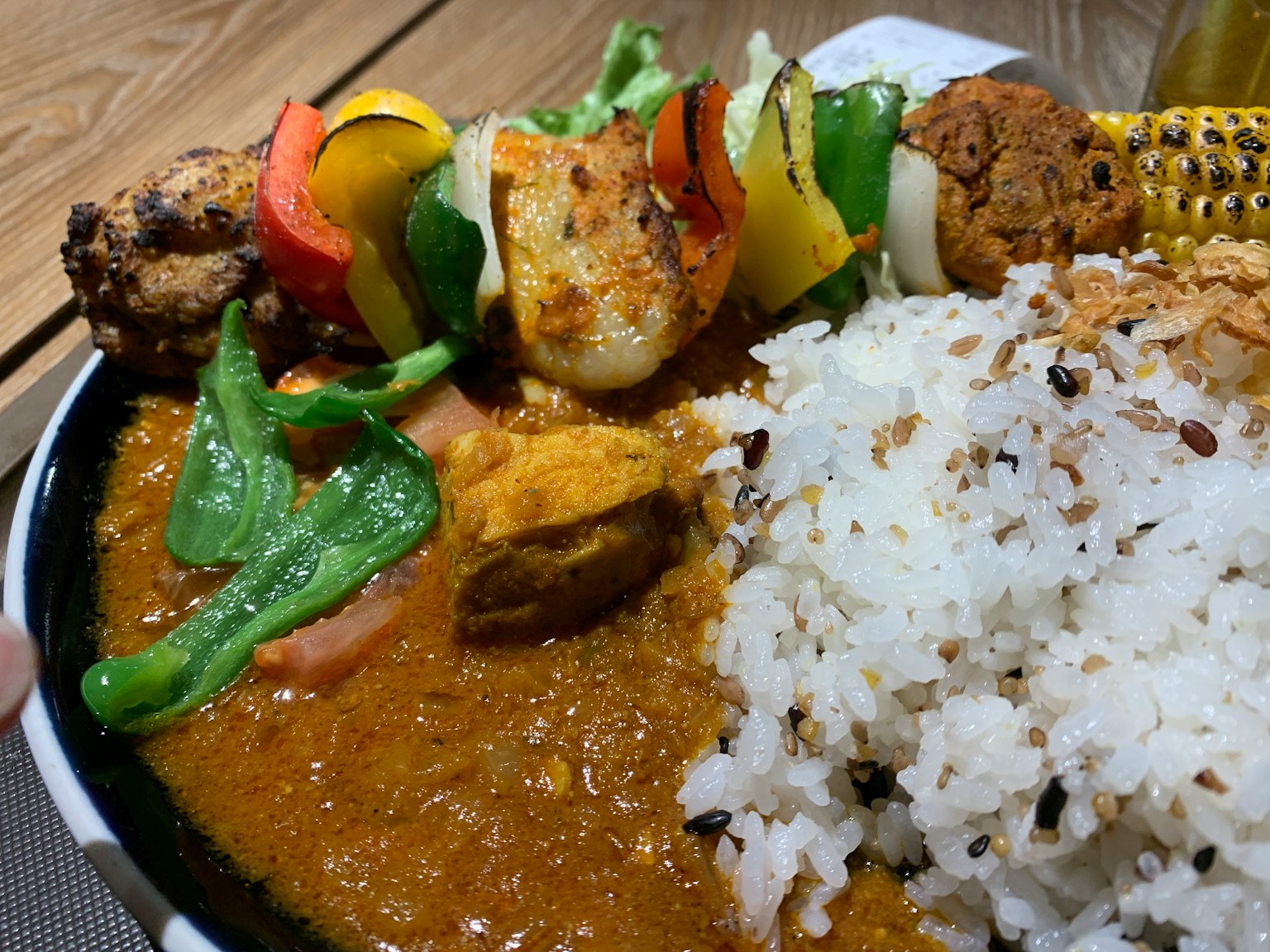Un plato vibrante de curry con arroz acompañado de verduras y carne en brochetas coloridas