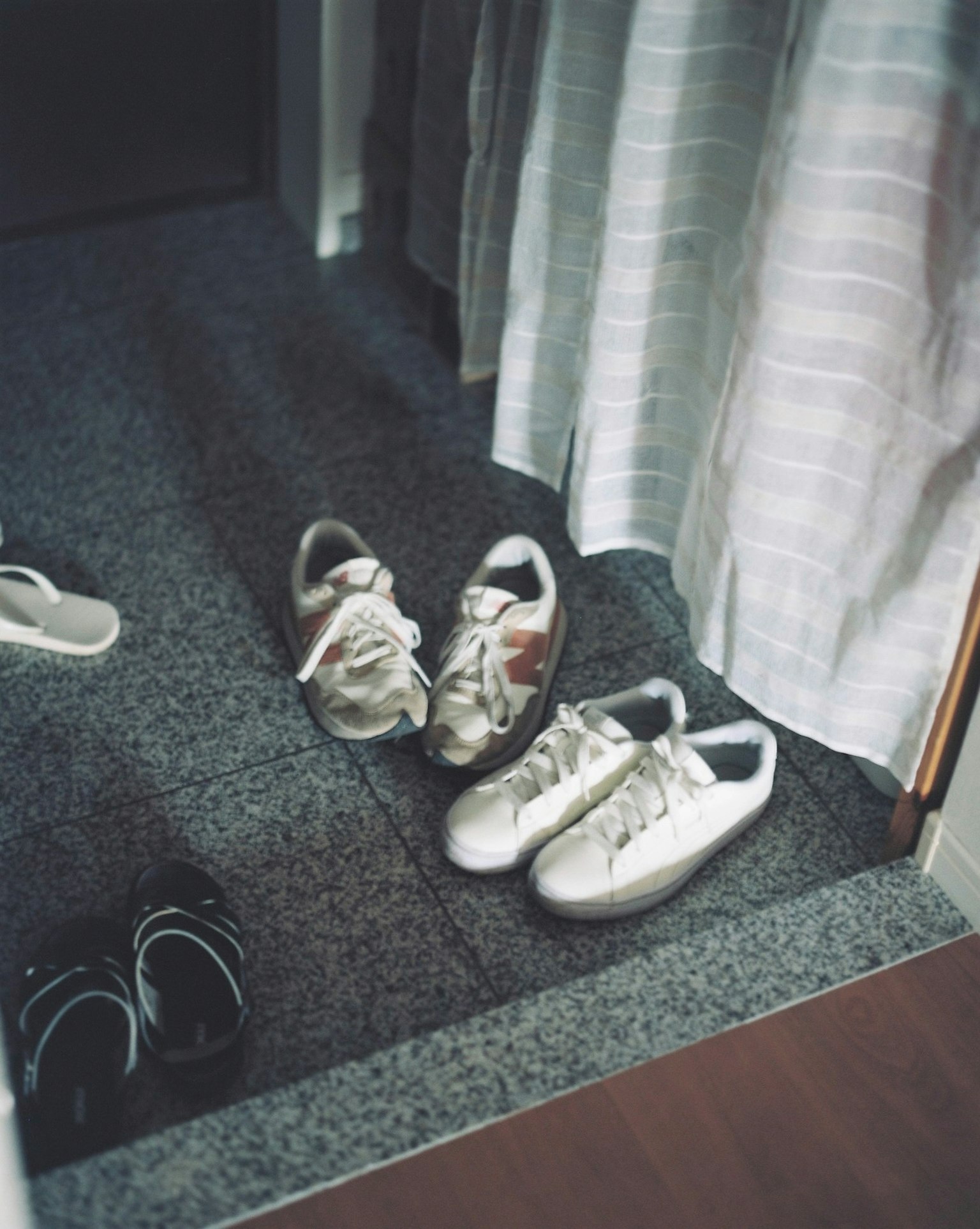 Sneakers bianche e sandali neri posati all'ingresso