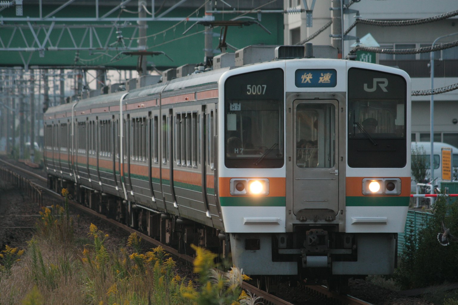 รถไฟญี่ปุ่นที่มีลายสีส้มและสีเขียวกำลังวิ่งอยู่บนราง