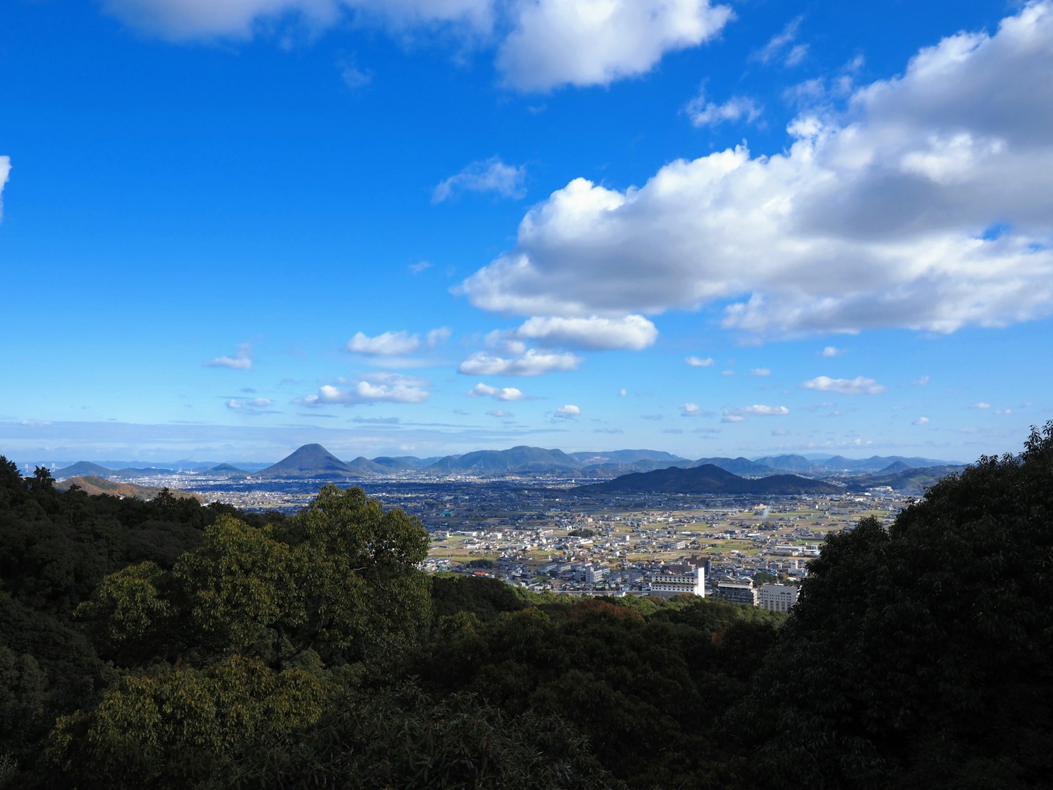 Pemandangan panorama pegunungan dan kota di bawah langit biru dengan awan putih