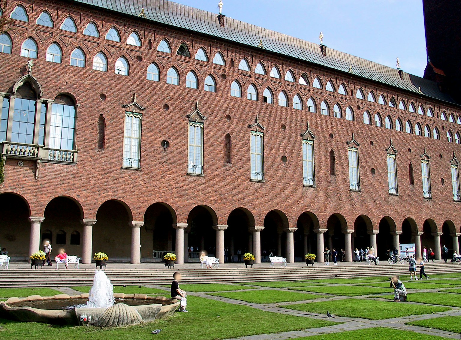 Un paesaggio con un edificio in mattoni rossi con colonne ad arco e una fontana
