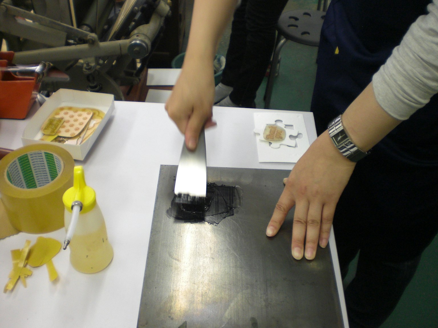 Applying black ink to a metal plate using a brush in a workshop