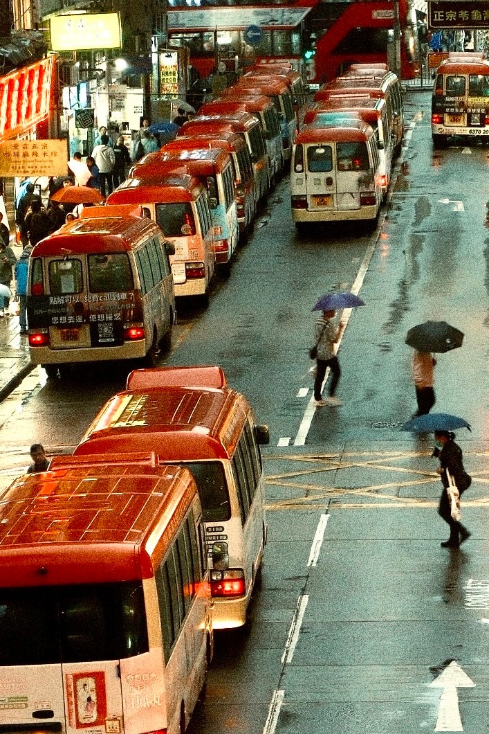 雨の路地に並ぶ赤いタクシーと歩行者のある街並み