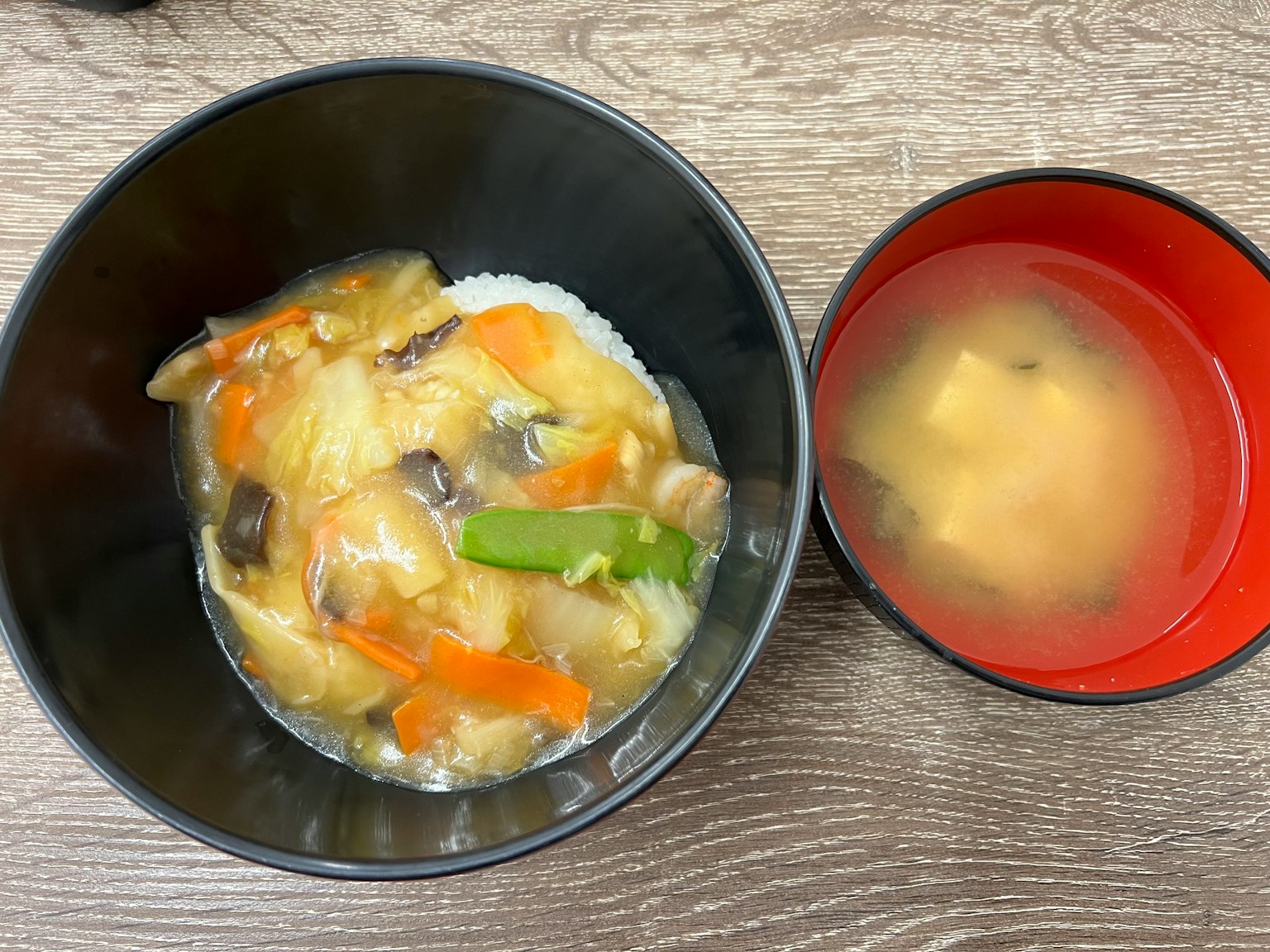 一碗米饭上面覆盖着美味的鸡肉和蔬菜酱，旁边是一碗红色的味噌汤