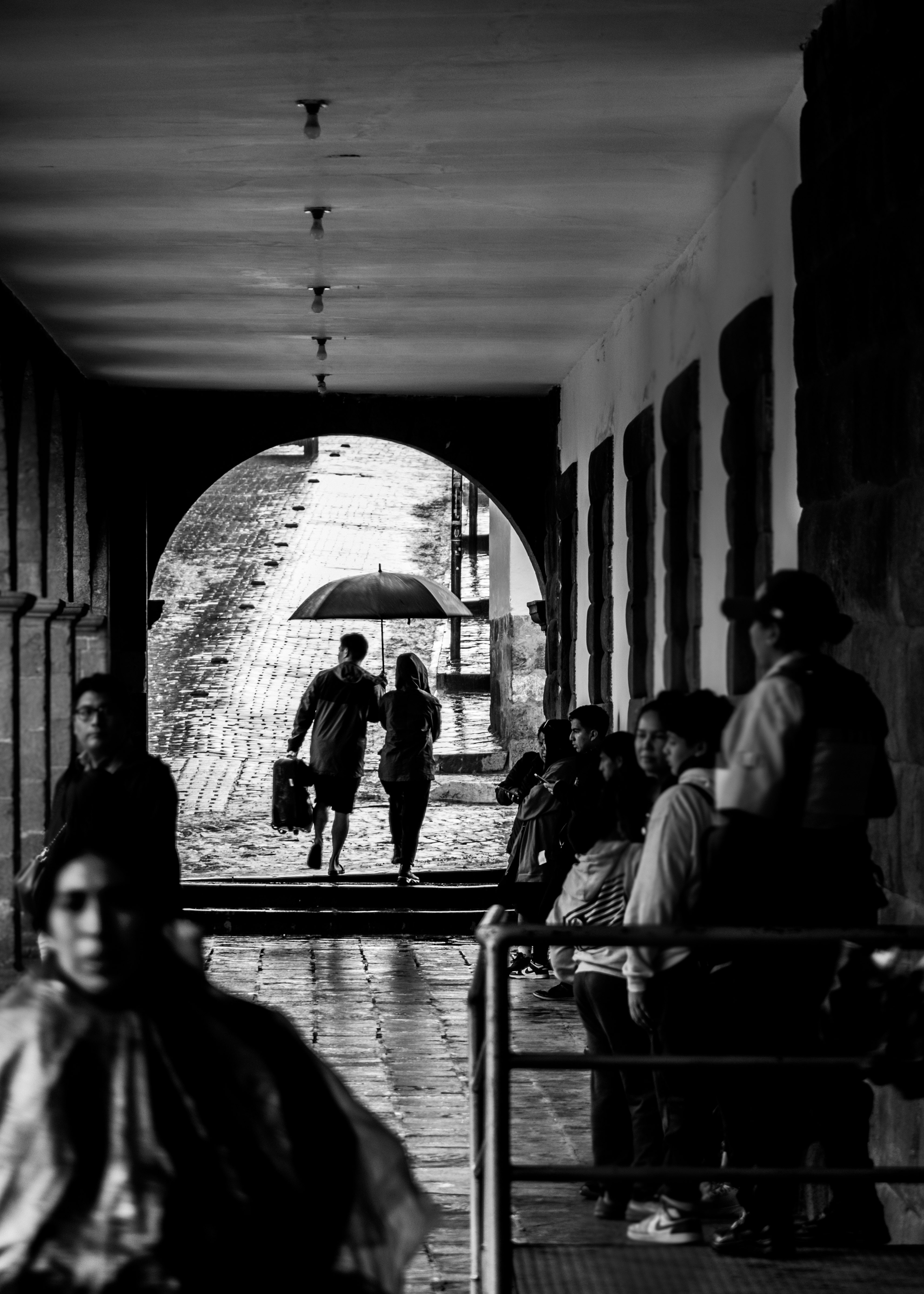 アーチ型の通路で傘をさす人々とベンチのある雨の駅前