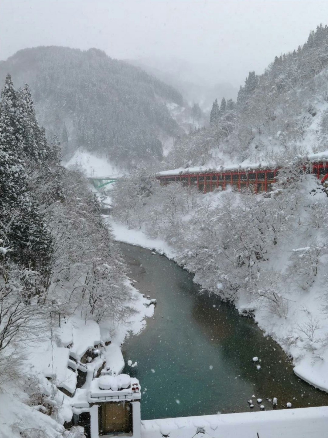 雪の渓谷を流れる川と赤い橋のある山間の風景