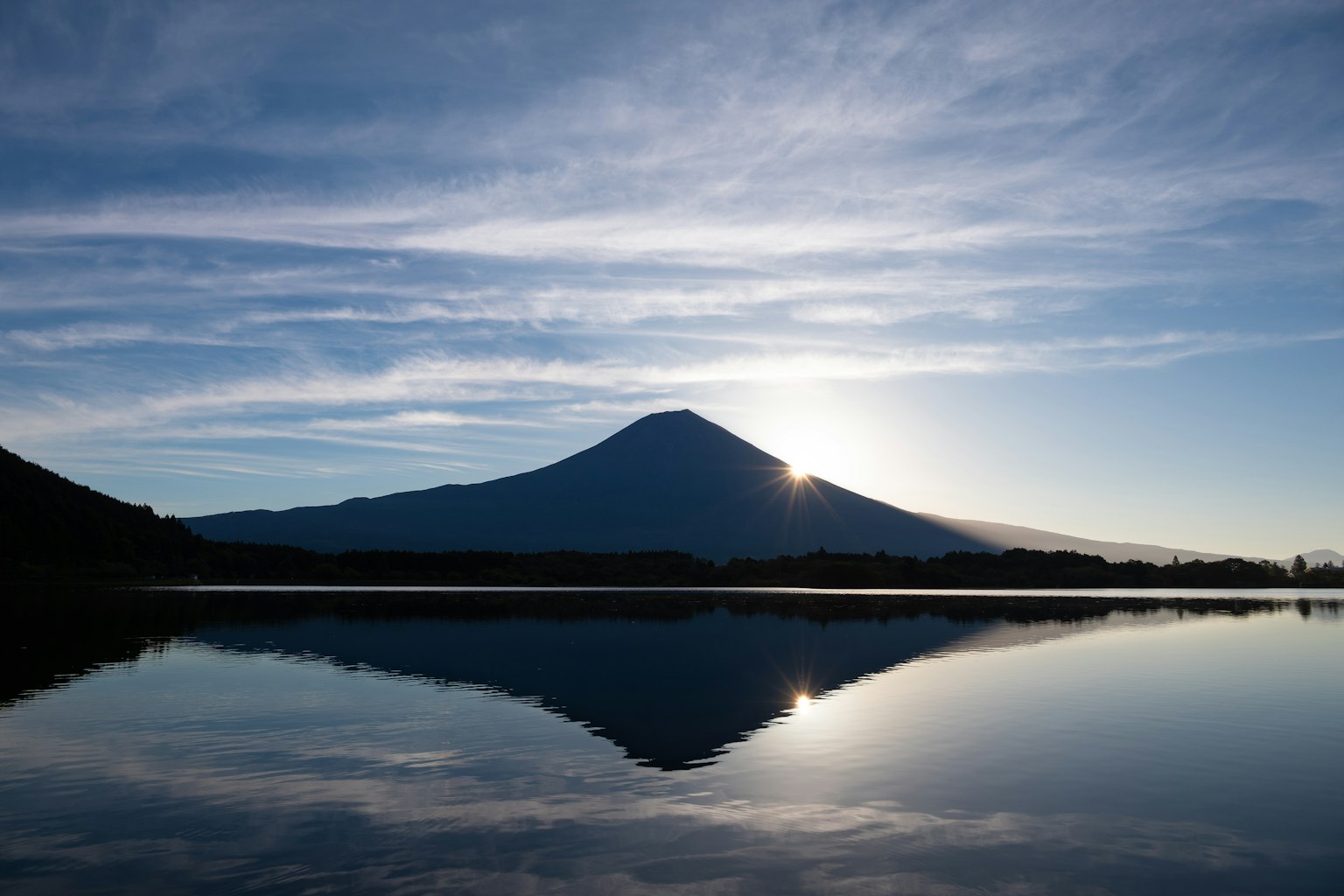 Silhouette of Mount Fuji reflected in a calm lake during sunrise
