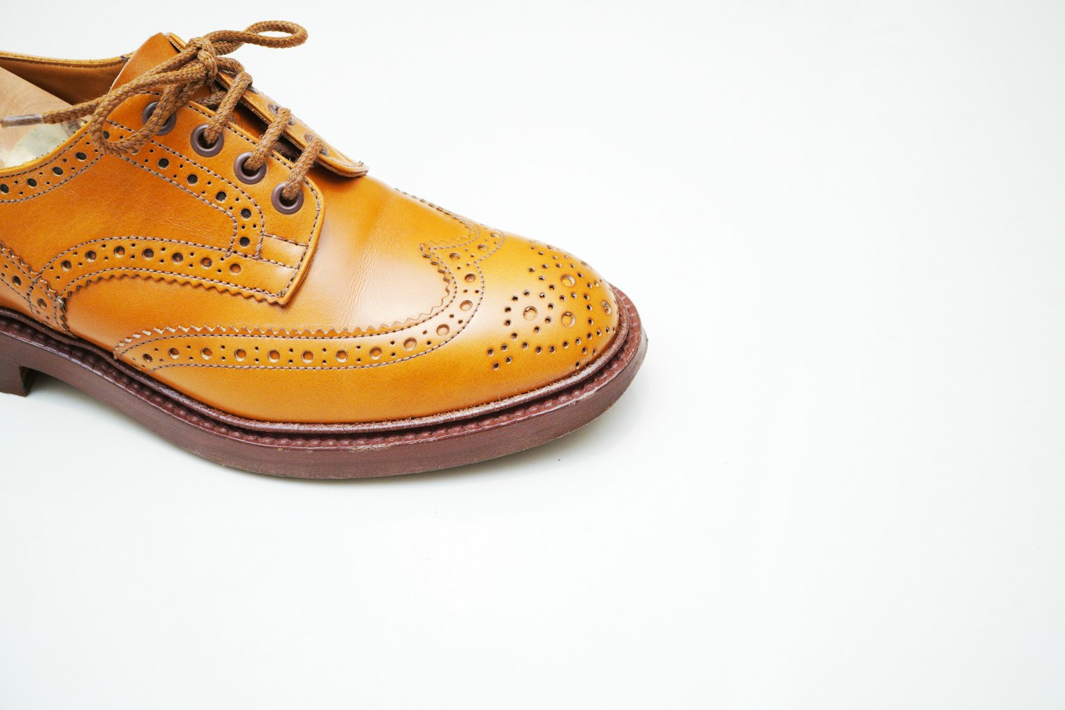 Primer plano de un zapato de cuero marrón claro con detalles de brogue sobre un fondo blanco