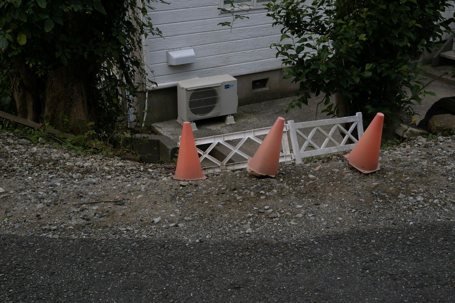 Scene of a gravel path with orange cones and a white fence