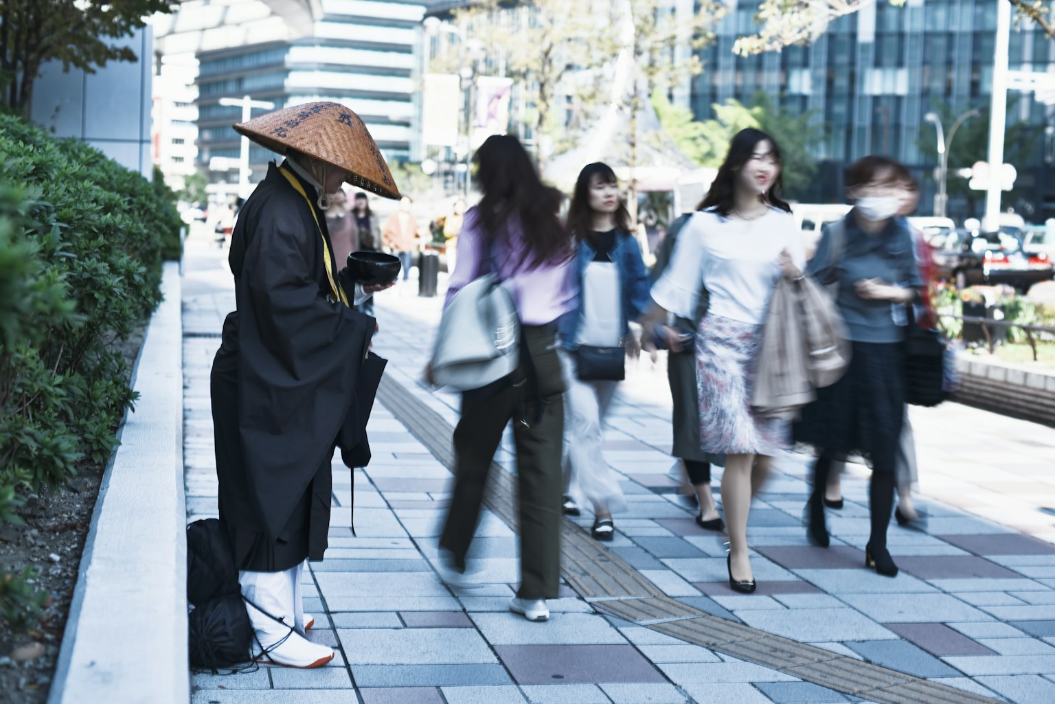 一位和尚坐在街上，周围是走动的人们，现代城市环境