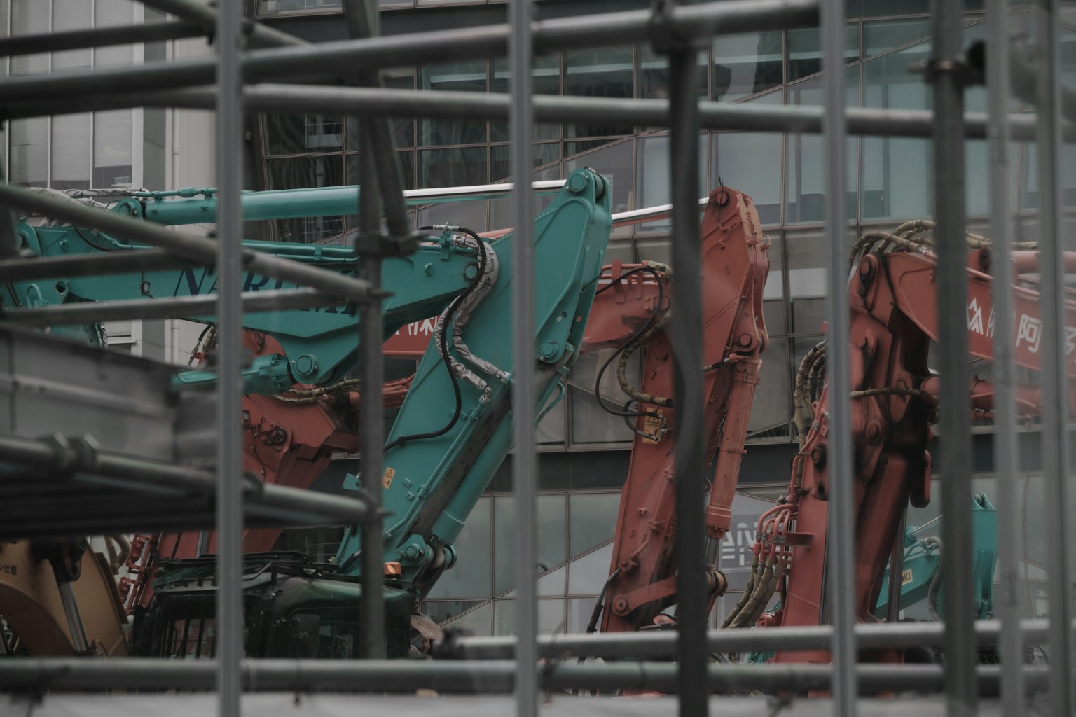 ภาพของไซต์ก่อสร้างที่มีแขนเครนสีเขียวและสีส้มที่มองเห็นได้