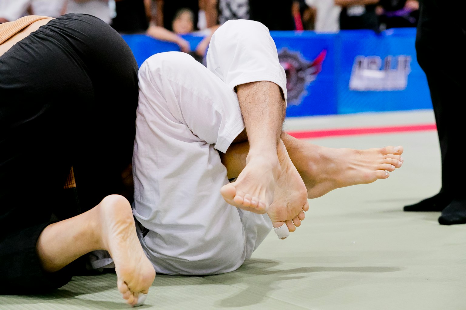 Two jiu-jitsu competitors grappling with feet prominently displayed