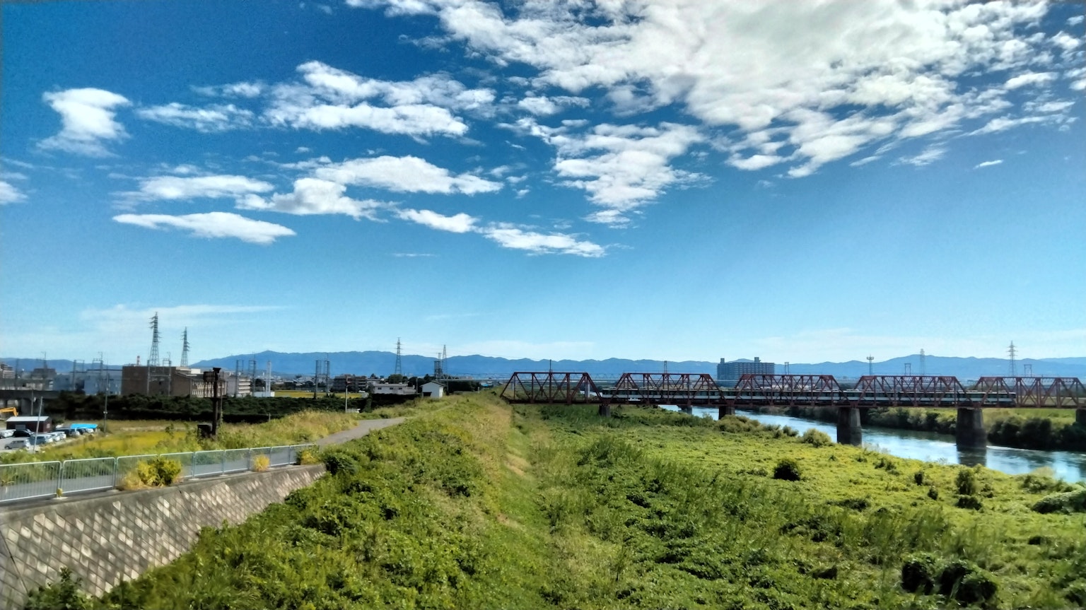 Landscape featuring a river and lush greenery under a blue sky with white clouds