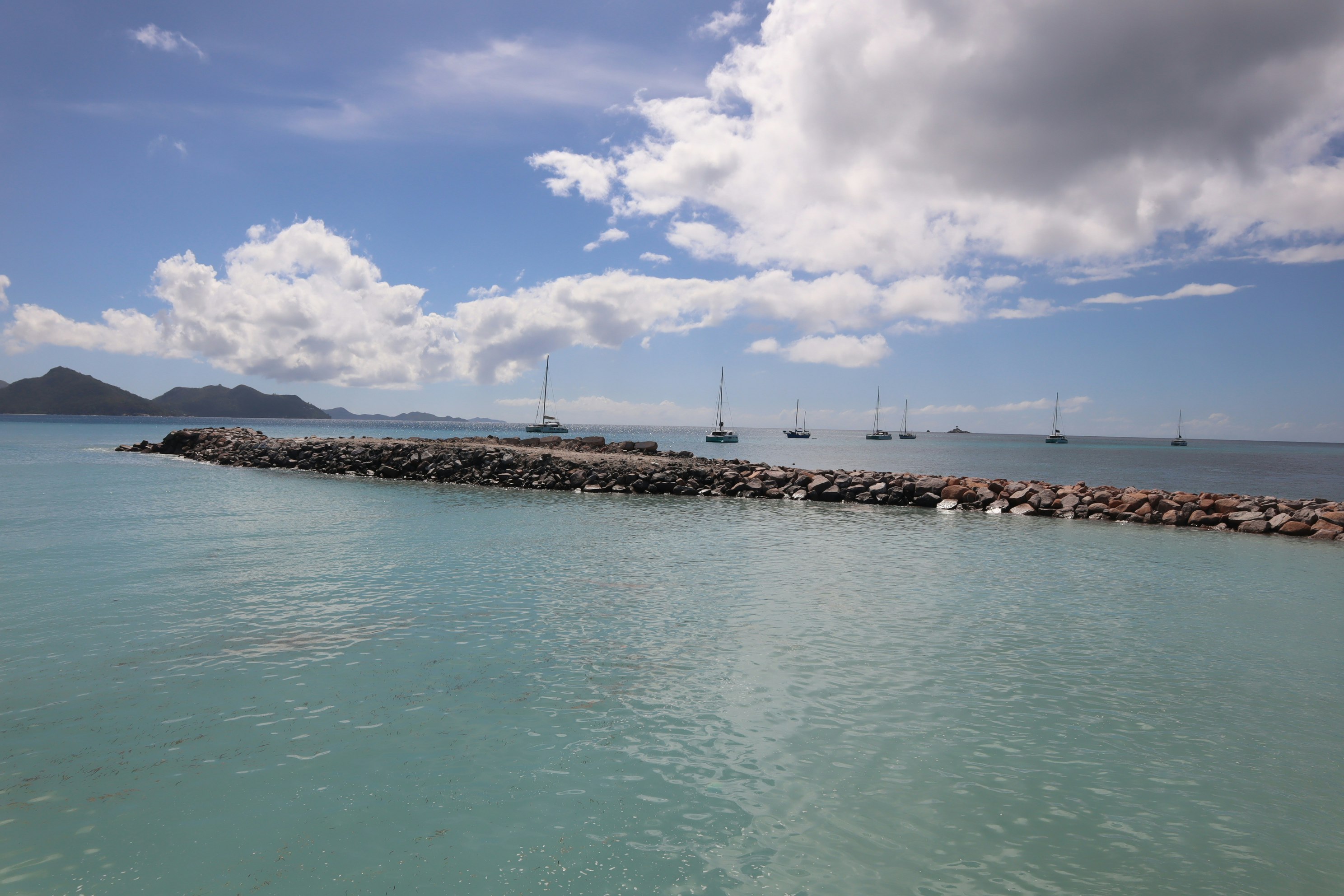 ทิวทัศน์ชายฝั่งเงียบสงบ มีเขื่อนกันคลื่นและเรือใบ