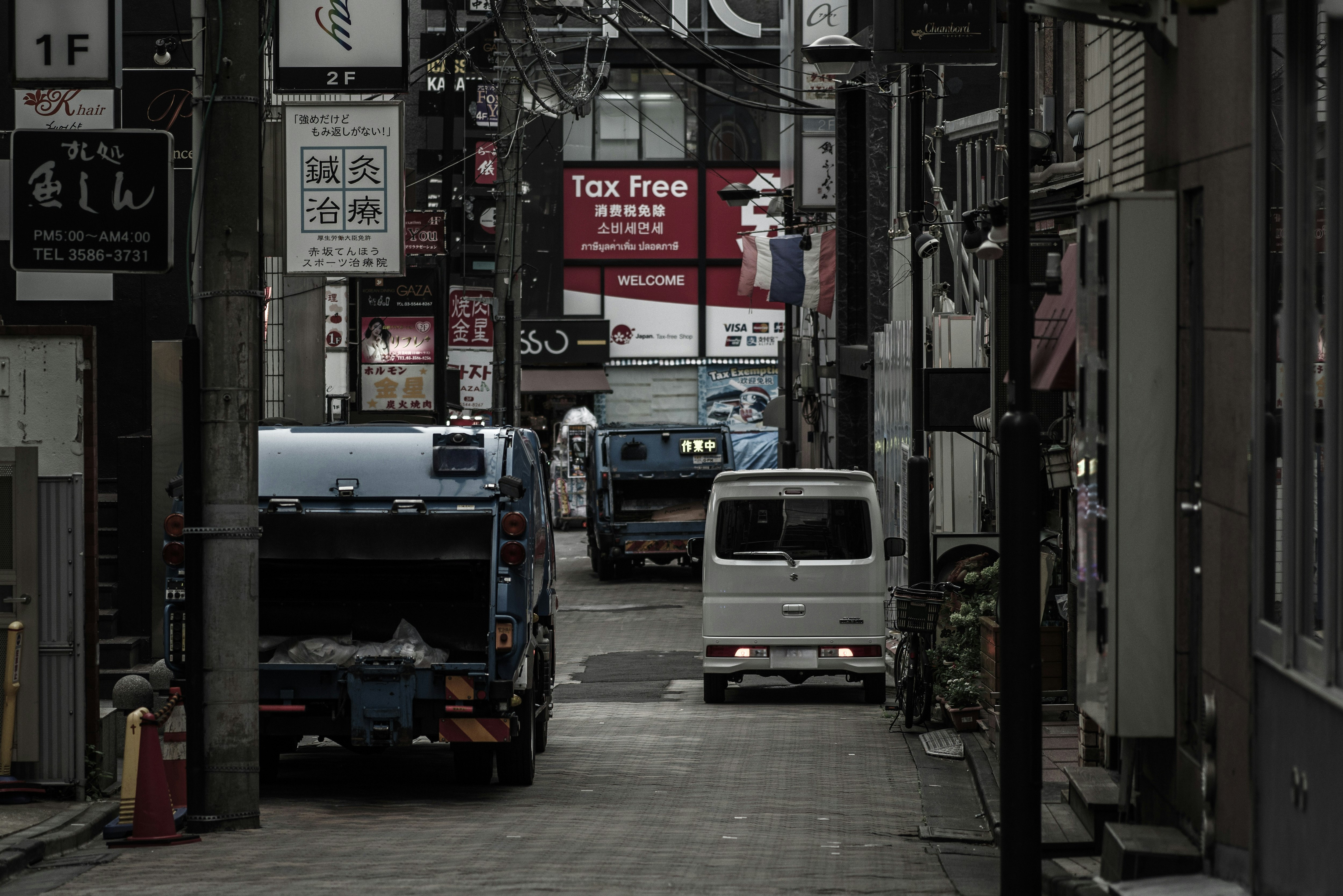 朝の路地に並ぶ車と看板のある商店街の通り