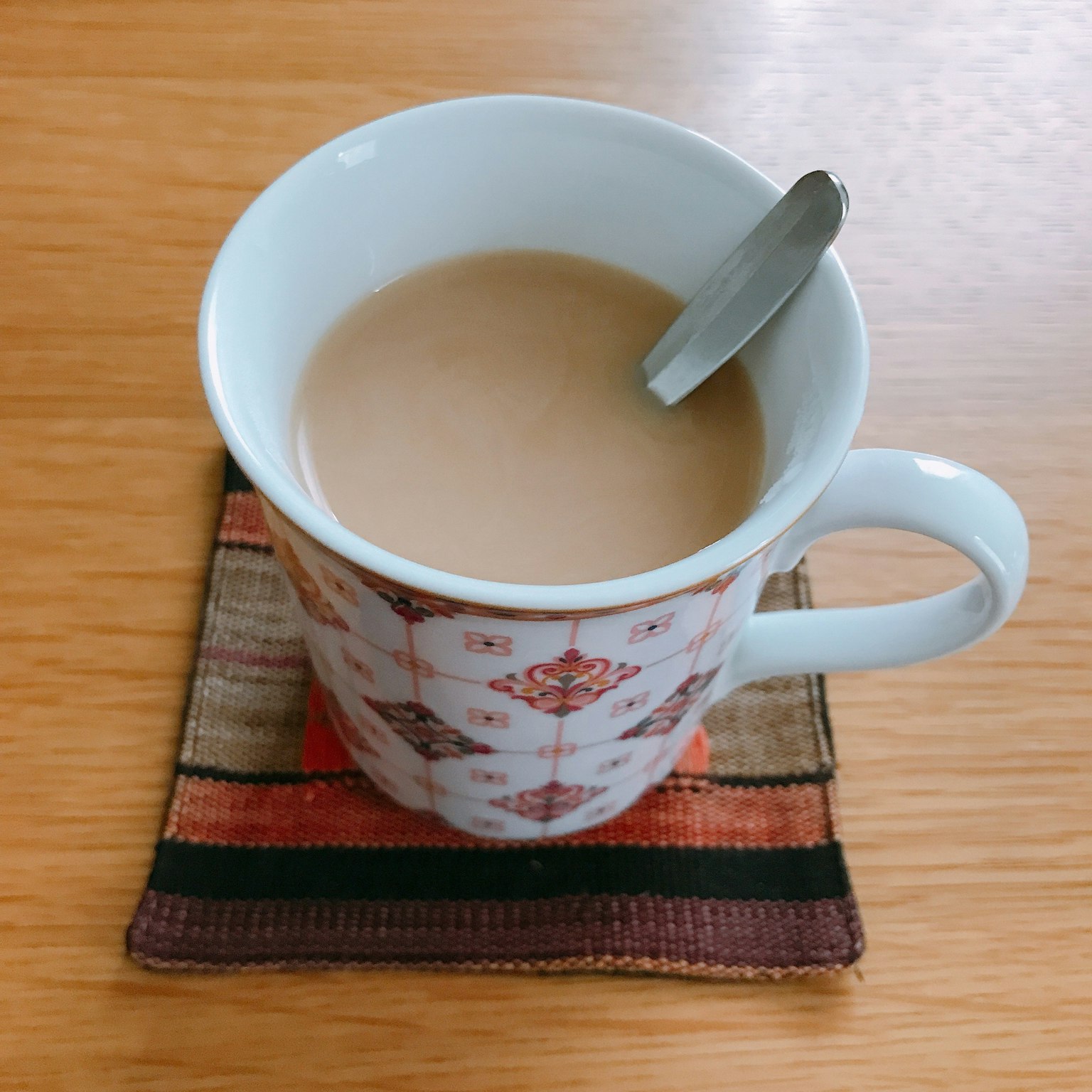 Sebuah cangkir putih dengan minuman hangat dan sendok di atas meja cokelat