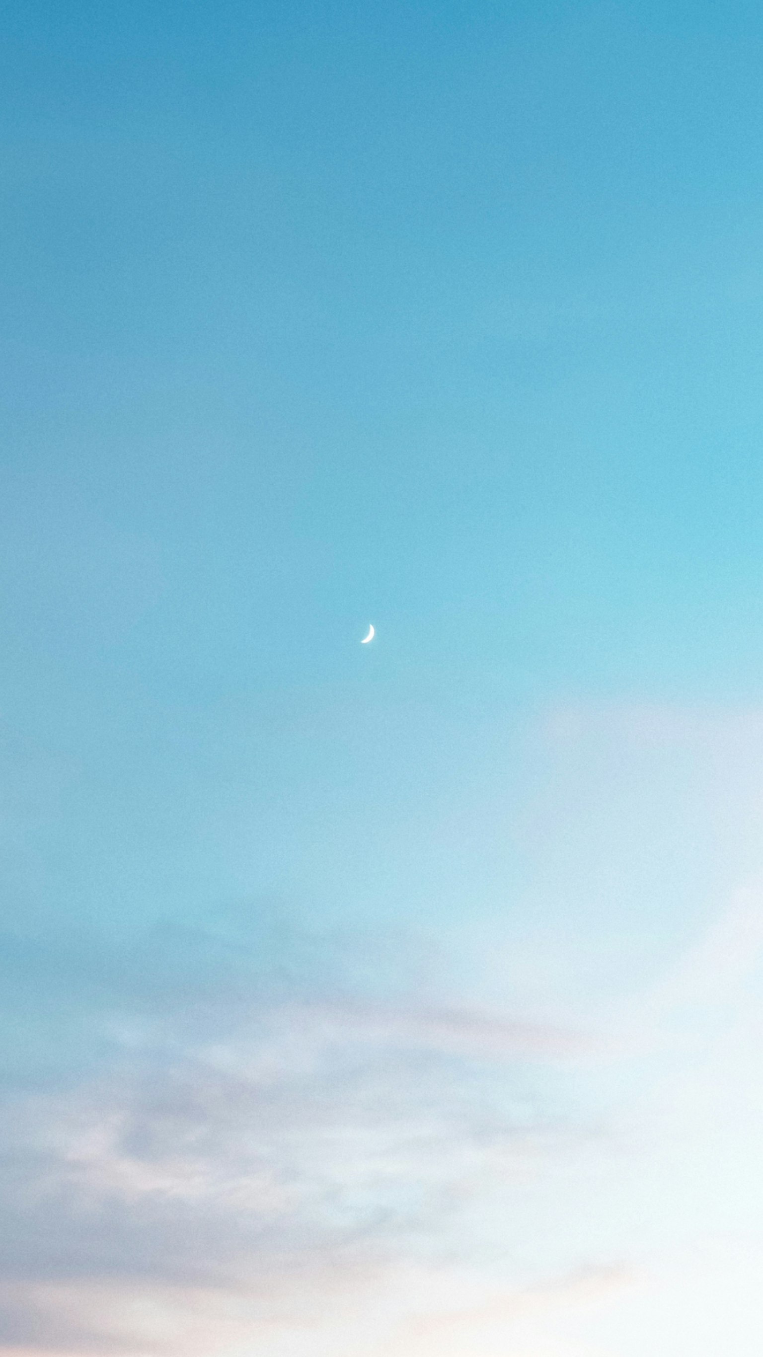 Un cielo azul sereno con nubes suaves y una pequeña luna creciente