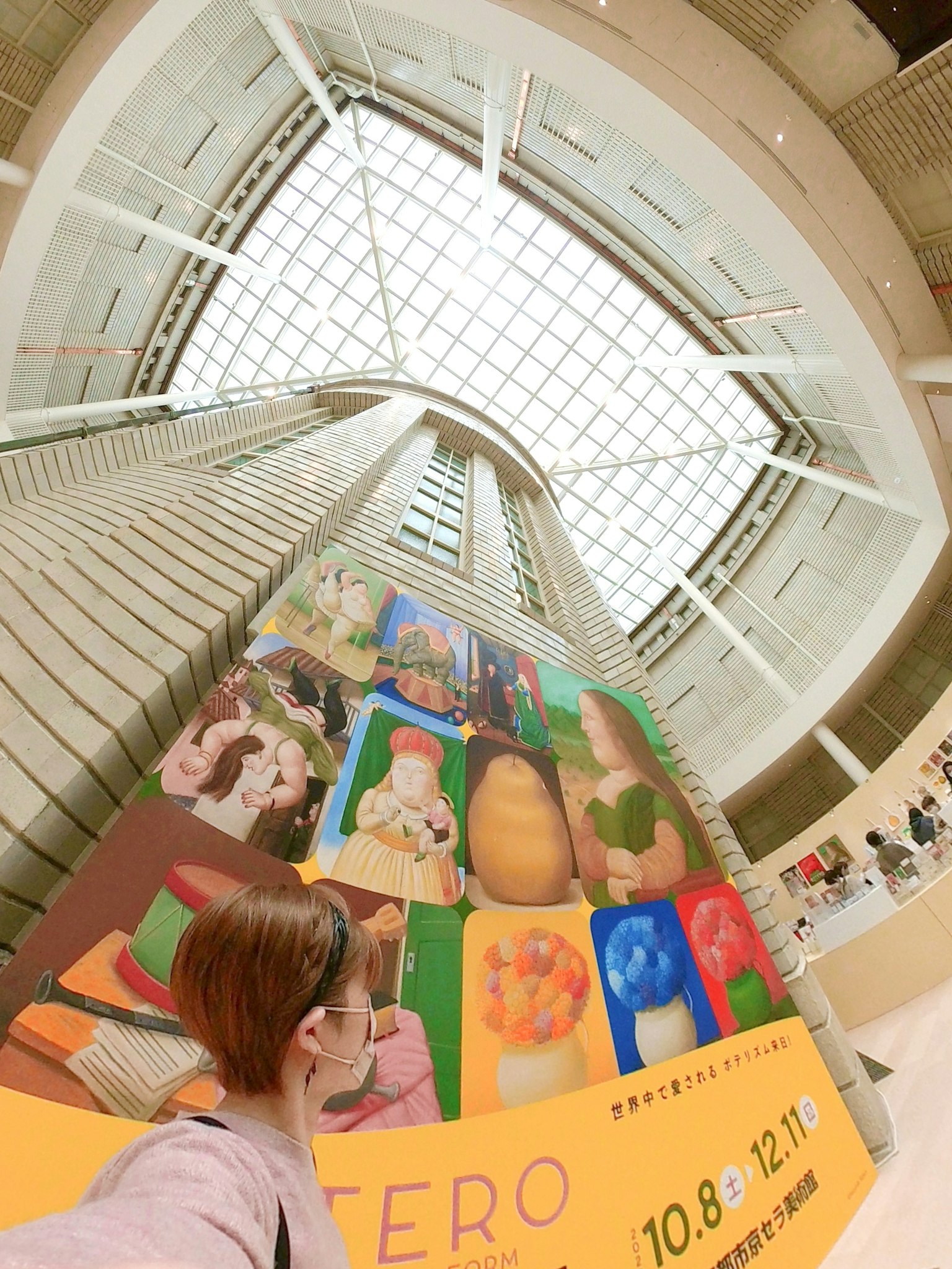 A person stands in front of a colorful exhibition poster inside a museum
