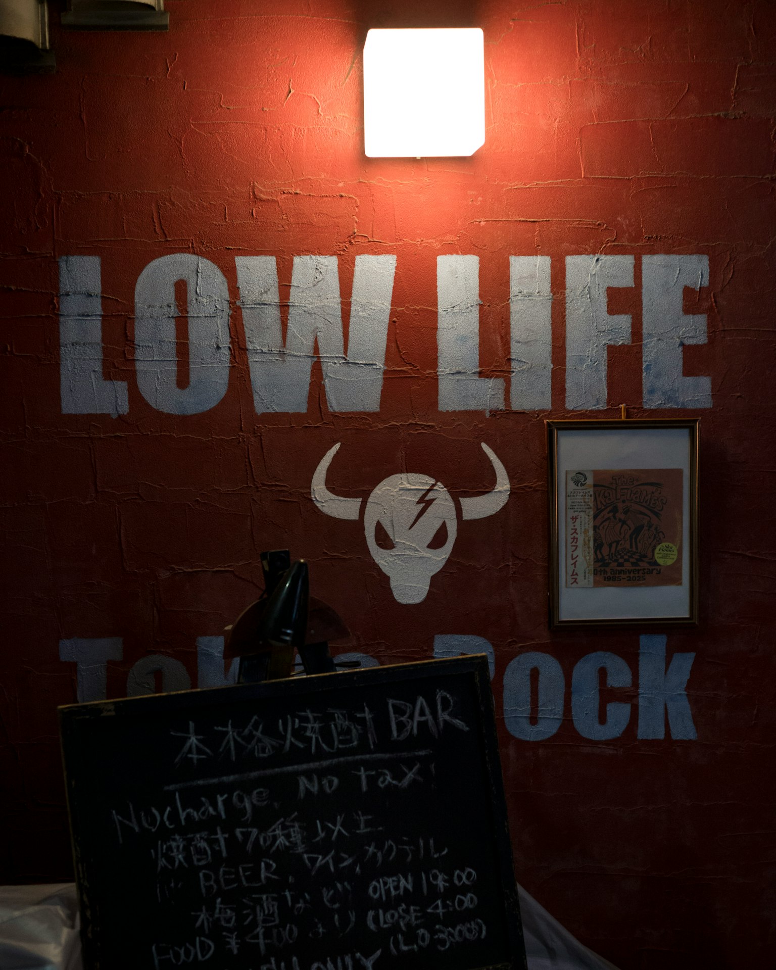 赤い壁に白い文字で「LOW LIFE」と書かれた看板と牛の頭のイラストがあるバーの外観