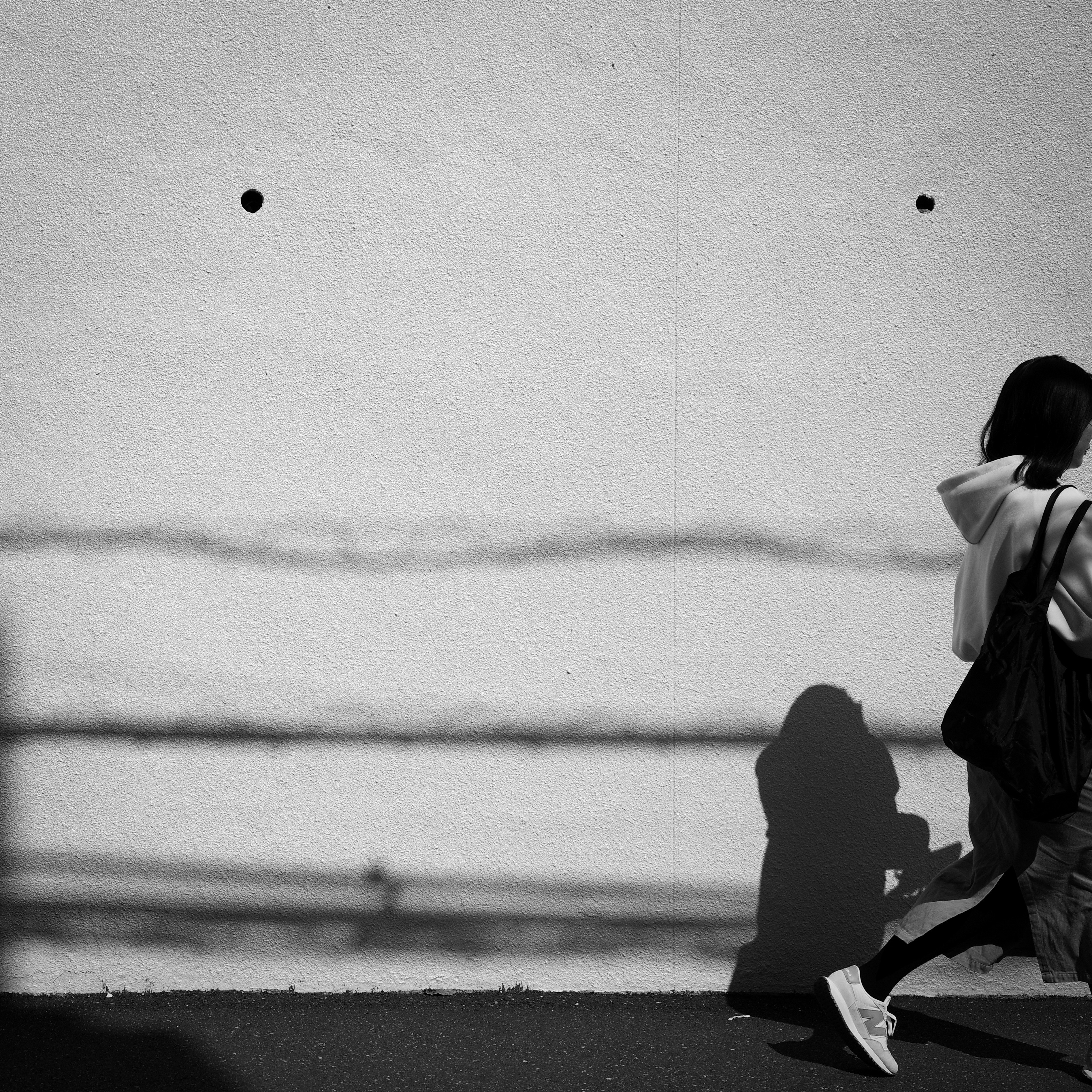 白い壁と影、東京の路上を歩く人物