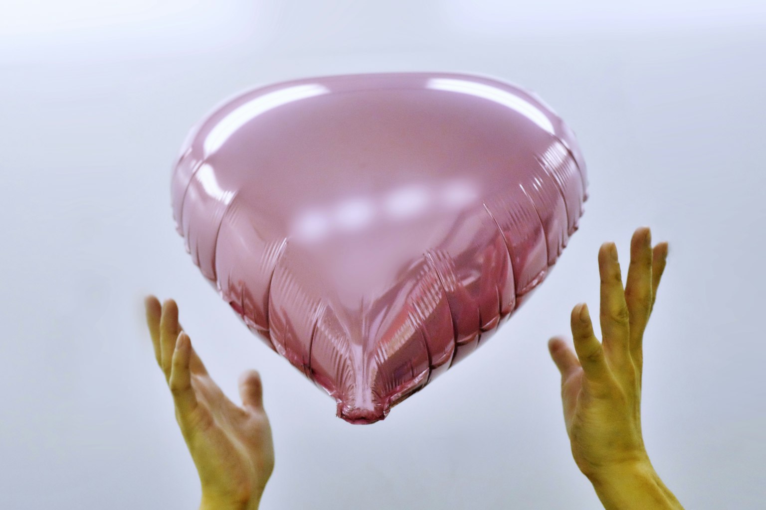Hände halten einen rosa herzförmigen Ballon