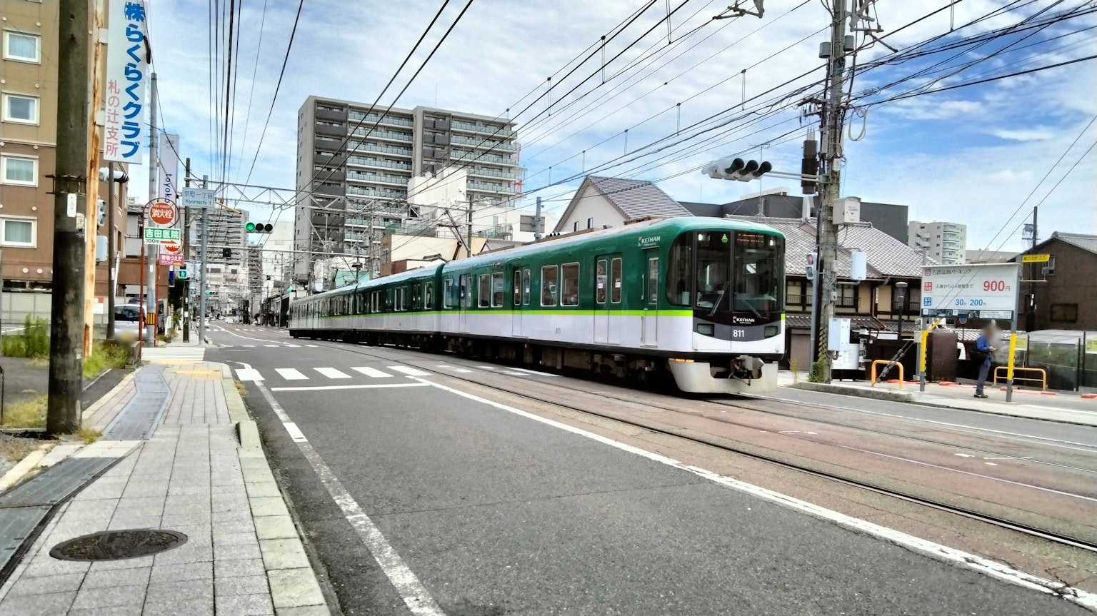一列綠色火車穿過城市街道，周圍有商業建築和住宅