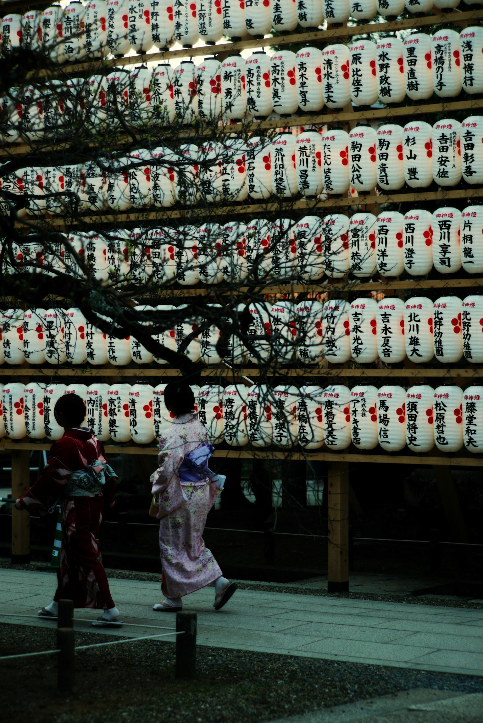 Women in kimonos walking in front of a wall of lanterns