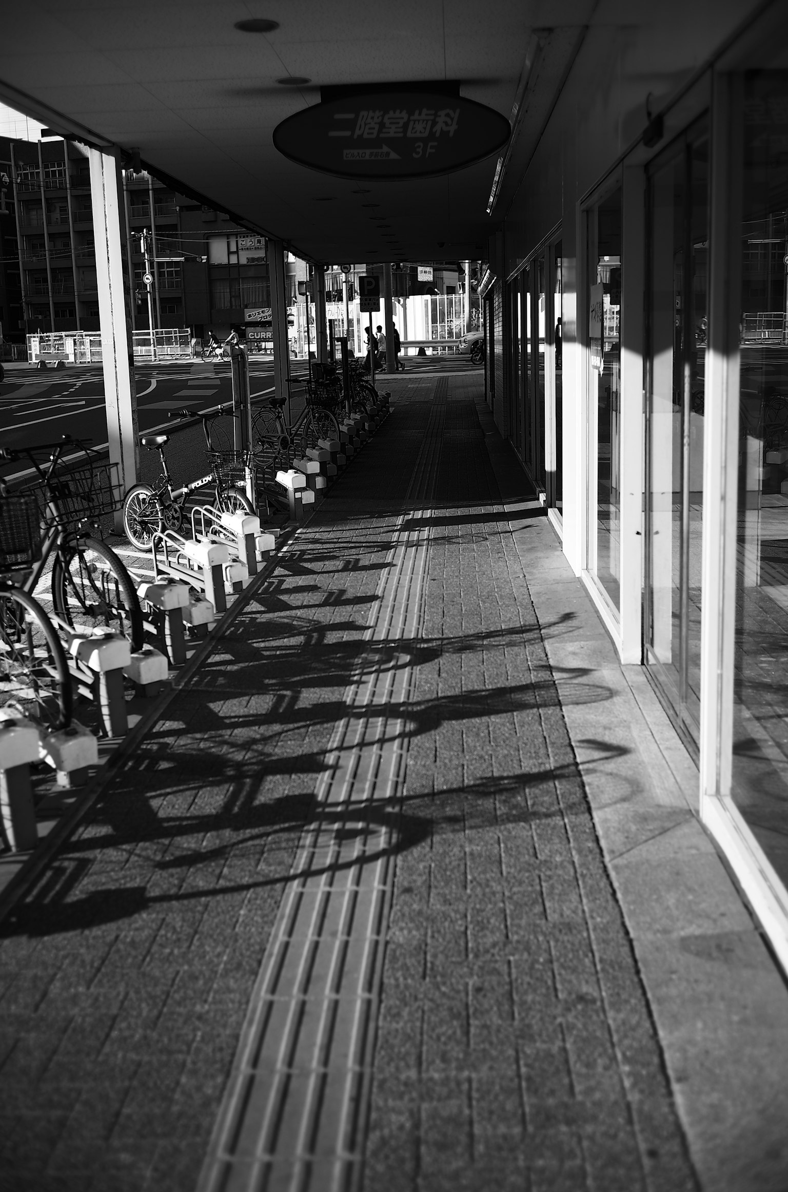 Vue en noir et blanc d'un trottoir avec des vélos et leurs ombres