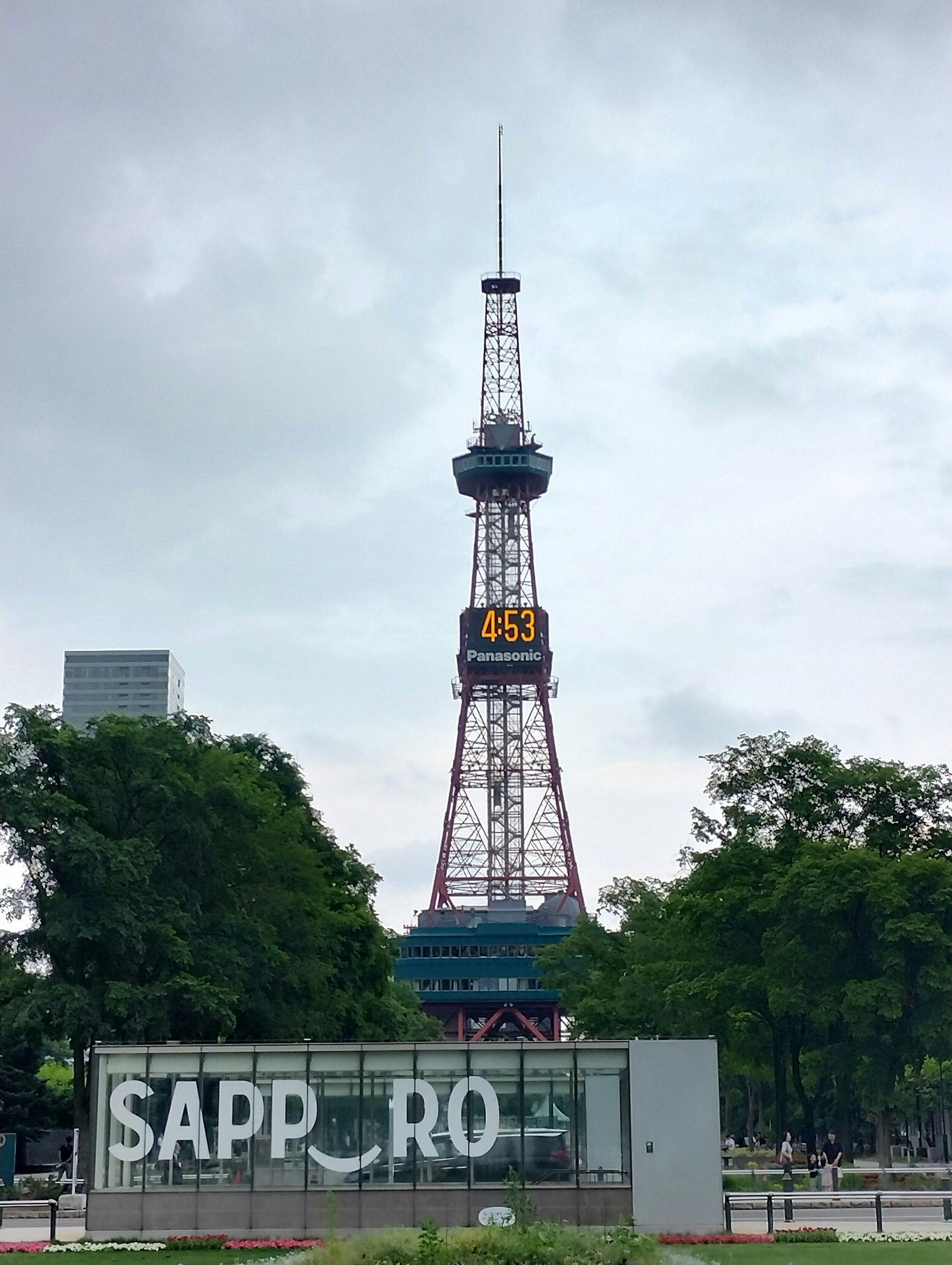 Torre de televisión de Sapporo que se eleva contra un cielo nublado con árboles verdes