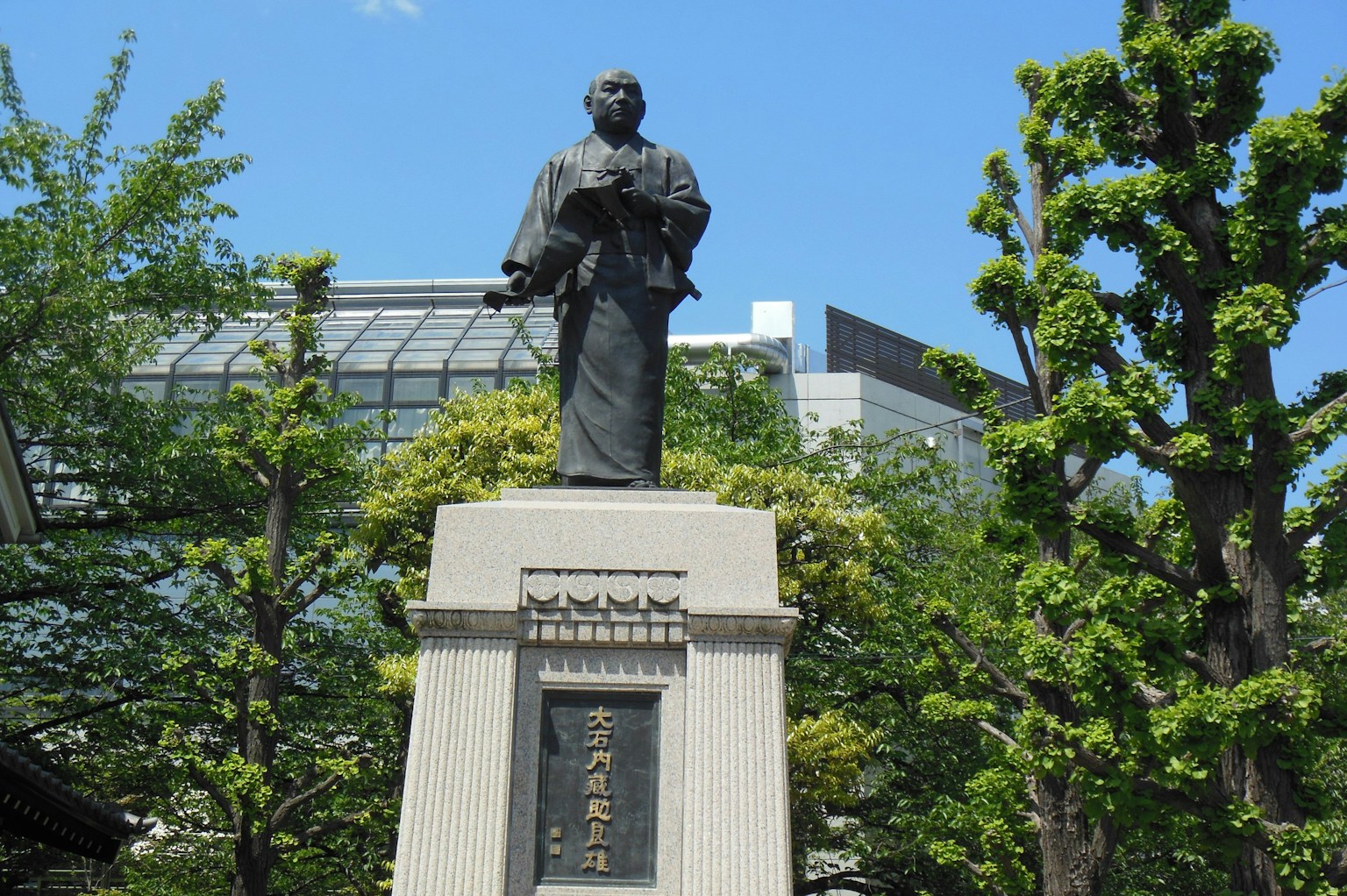 Patung berkostum kimono di bawah langit biru dengan latar belakang hijau subur